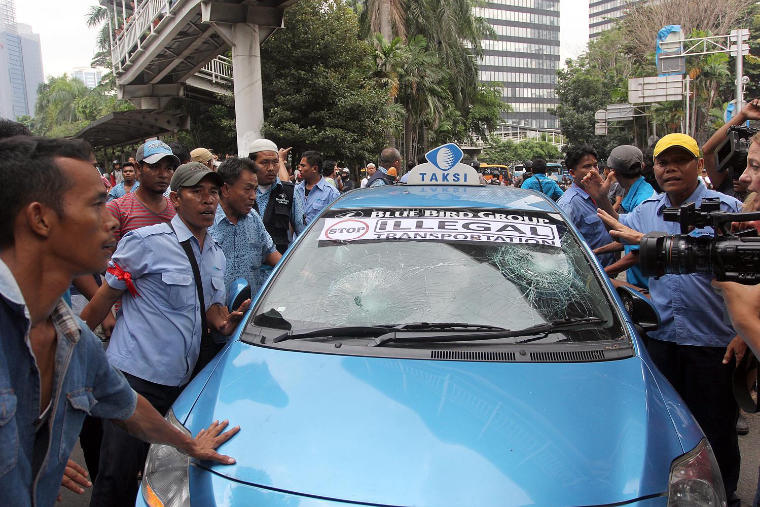 Sebuah mobil taksi yang menolak ikut aksi unjuk rasa dihadang dan dihancurkan oleh para pengemudi taksi lainnya di Jalan Sudirman-Thamrin, Jakarta, Selasa, (22/3).