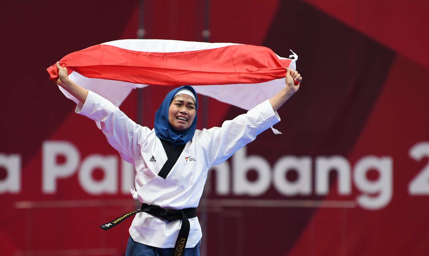 Atlet Taekwondo putri Indonesia Rosmaniar Defia berlari membawa bendera merah putih usai menang melawan Taekwondoin putri Iran Marjan Salahshouri pada partai final poomsae individu pada Asian Games 2018 di Jakarta Convention Center (JCC), Defia menang dan memperoleh medali emas untuk Indonesia. Minggu (19/8).