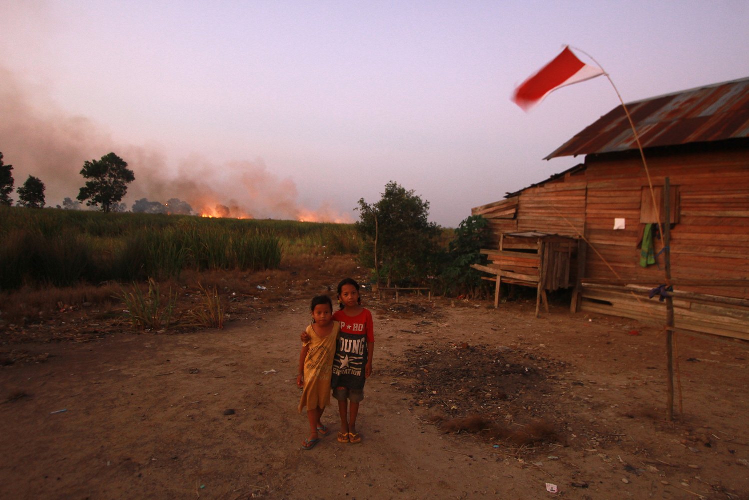 Anak-anak berpose di halaman rumah dengan latar belakang kebakaran lahan gambut di Kecamatan Bati-Bati, Kabupaten Tanah Laut, Kalimantan Selatan, Minggu (1/9/2019). 