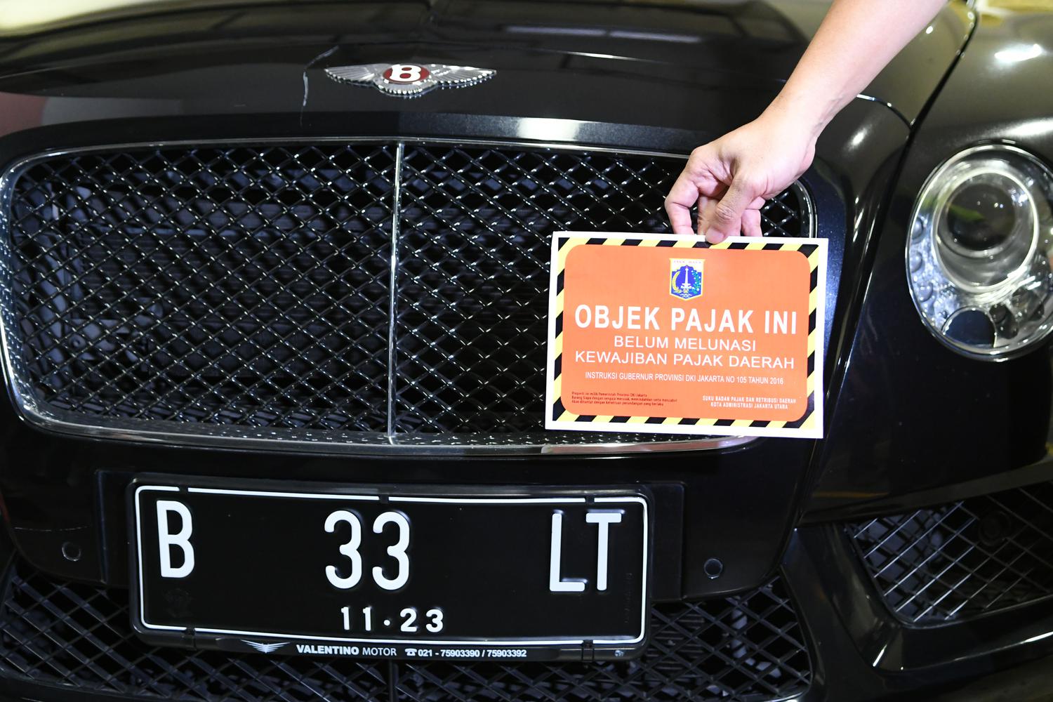 Petugas Samsat Jakarta Utara menunjukkan stiker 'Objek Pajak' di depan mobil mewah Bentley saat razia supervisi pencegahan pajak mobil mewah di Apartemen Regatta, Jakarta Utara di Jakarta, Kamis (5/12/2019). 