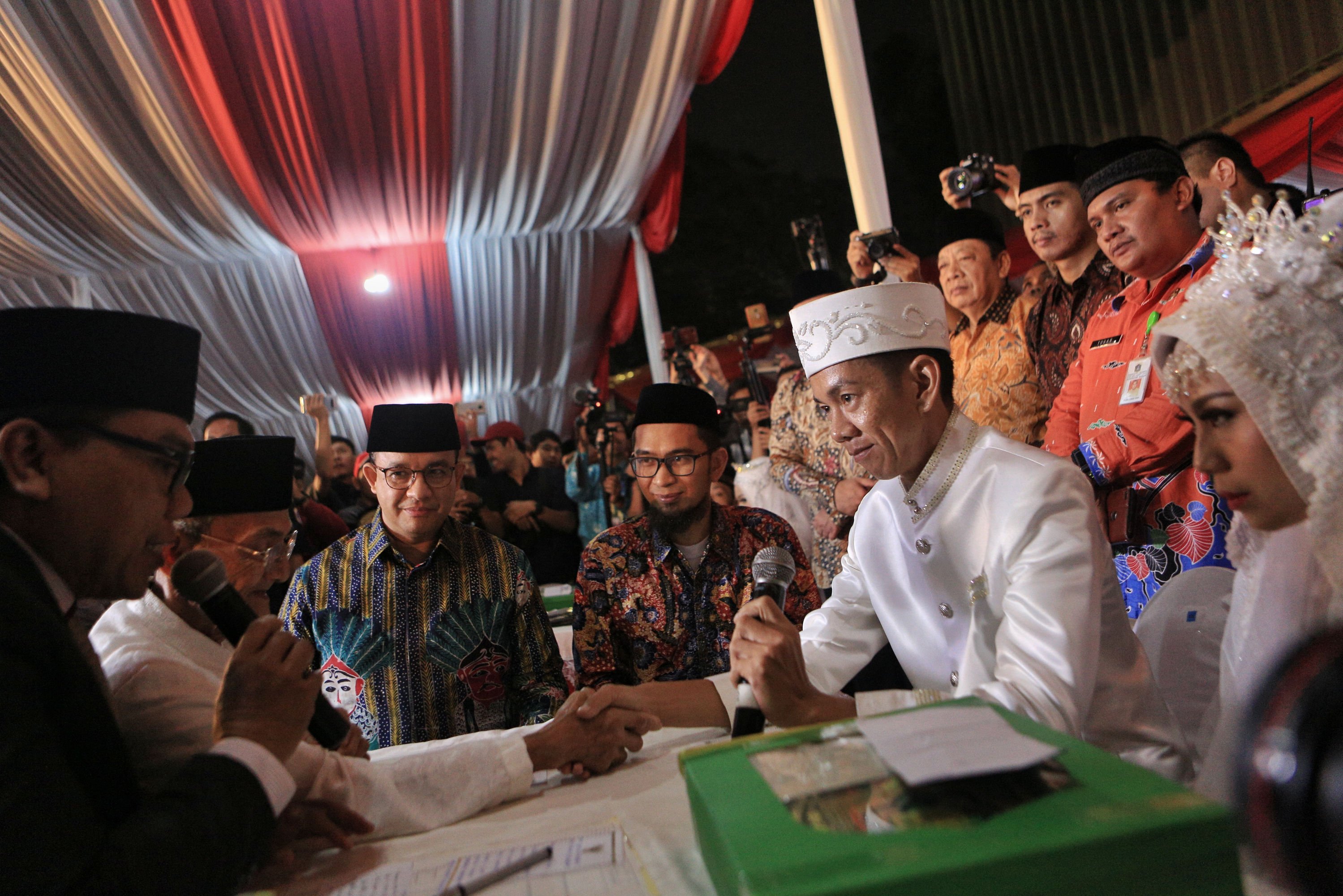Gubernur DKI Jakarta Anies Baswedan (kiri) menjadi saksi pernikahan saat acara nikah massal di halaman Balai Kota, Jakarta, Selasa (31/12/2019). 