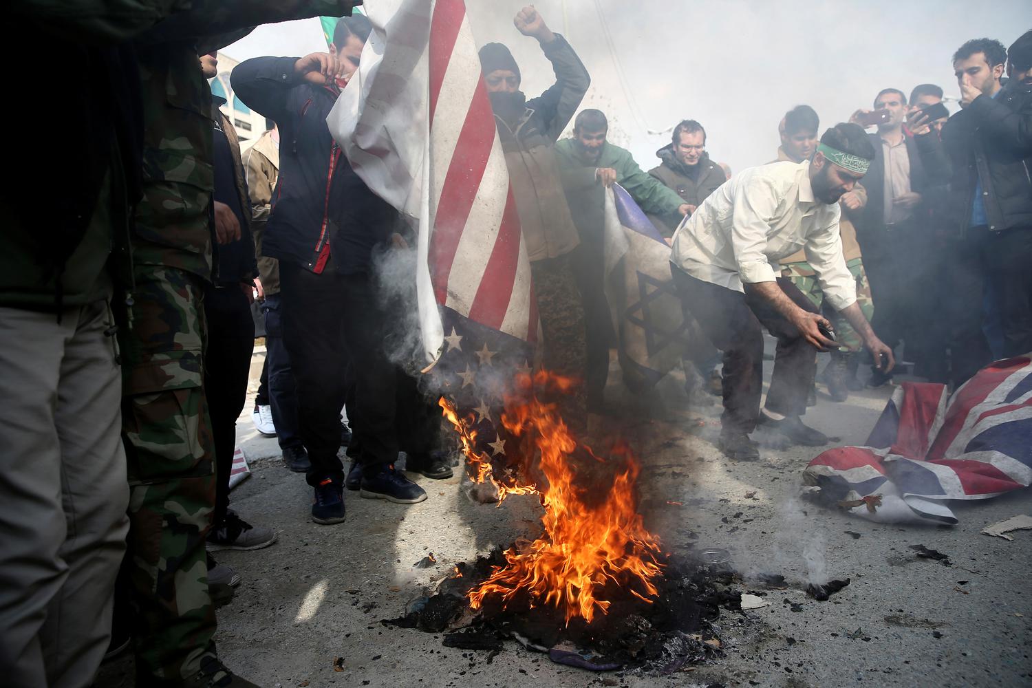 Demonstran membakar bendera Amerika Serikat, Israel dan Inggris saat aksi protes menentang pembunuhan Mayor Jenderal Iran Qassem Soleimani, kepala pasukan elit Quds, dan komandan milisi Irak Abu Mahdi al-Muhandis, yang tewas saat serangan udara di bandara Baghdad, di Teheran, Iran, Jumat (3/1/2020).