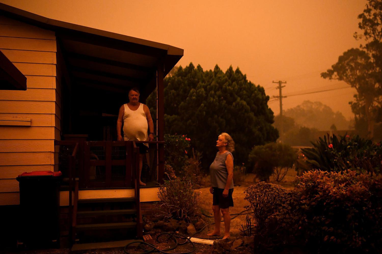 Nancy Allen dan Brian Allen berdiri di luar saat selang taman membasahi rumah saat angin kencang mendorong asap dan abu dari kebakaran Currowan menuju Nowra, New South Wales, Australia, Sabtu (4/1/2020).