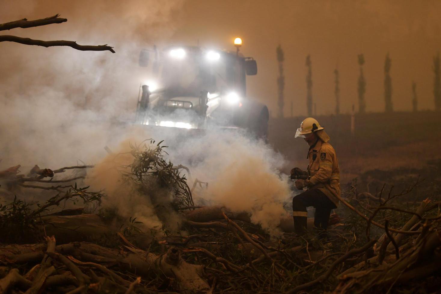 Pohon karet yang terbakar ditebang agar tidak jatuh di atas mobil di Corbago, ketika kebakaran hutan kembali terjadi di New South Wales, Australia, Minggu (5/1/2020).