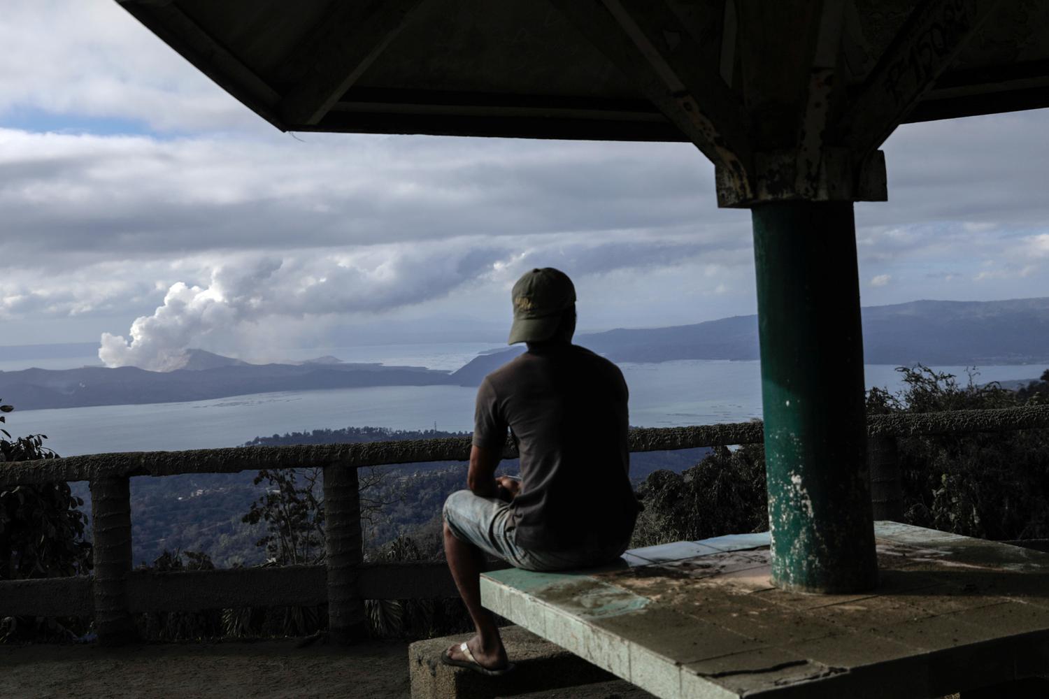 Seorang pria memperhatikan Gunung Berapi Taal yang meletus dari sebuah taman di Kota Tagaytay, Filipina, Selasa (14/1/2020).