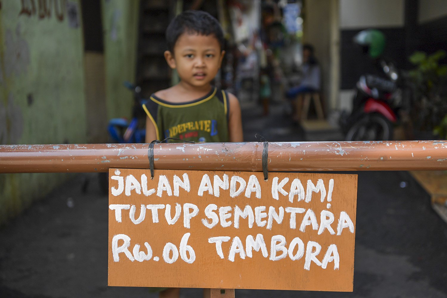 Seorang bocah berdiri di belakang portal karantina wilayah di kawasan Tambora, Jakarta. Warga setempat memberlakukan karantina wilayah secara mandiri dengan menutup beberapa akses jalan masuk perkampungan serta meningkatkan keamanan untuk mencegah penyebaran COVID-19. \r\n
