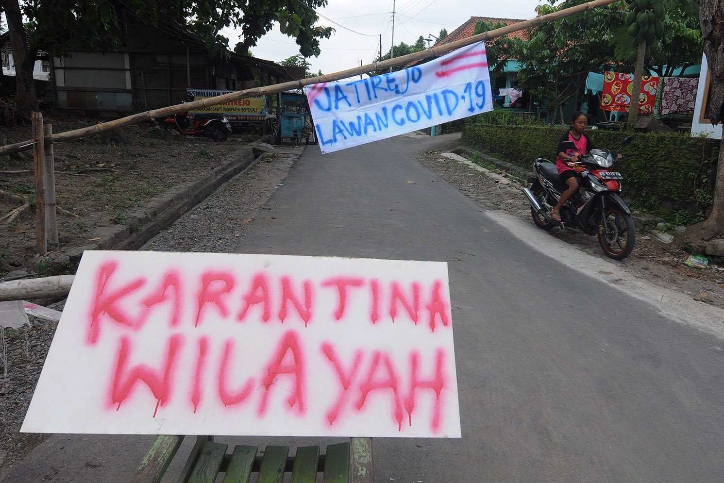 Warga melintas di dekat portal karantina wilayah di Sawit, Boyolali, Jawa Tengah. Warga setempat memberlakukan karantina wilayah secara mandiri dengan menutup beberapa akses jalan masuk perkampungan serta meningkatkan keamanan untuk mencegah penyebaran COVID-19. 