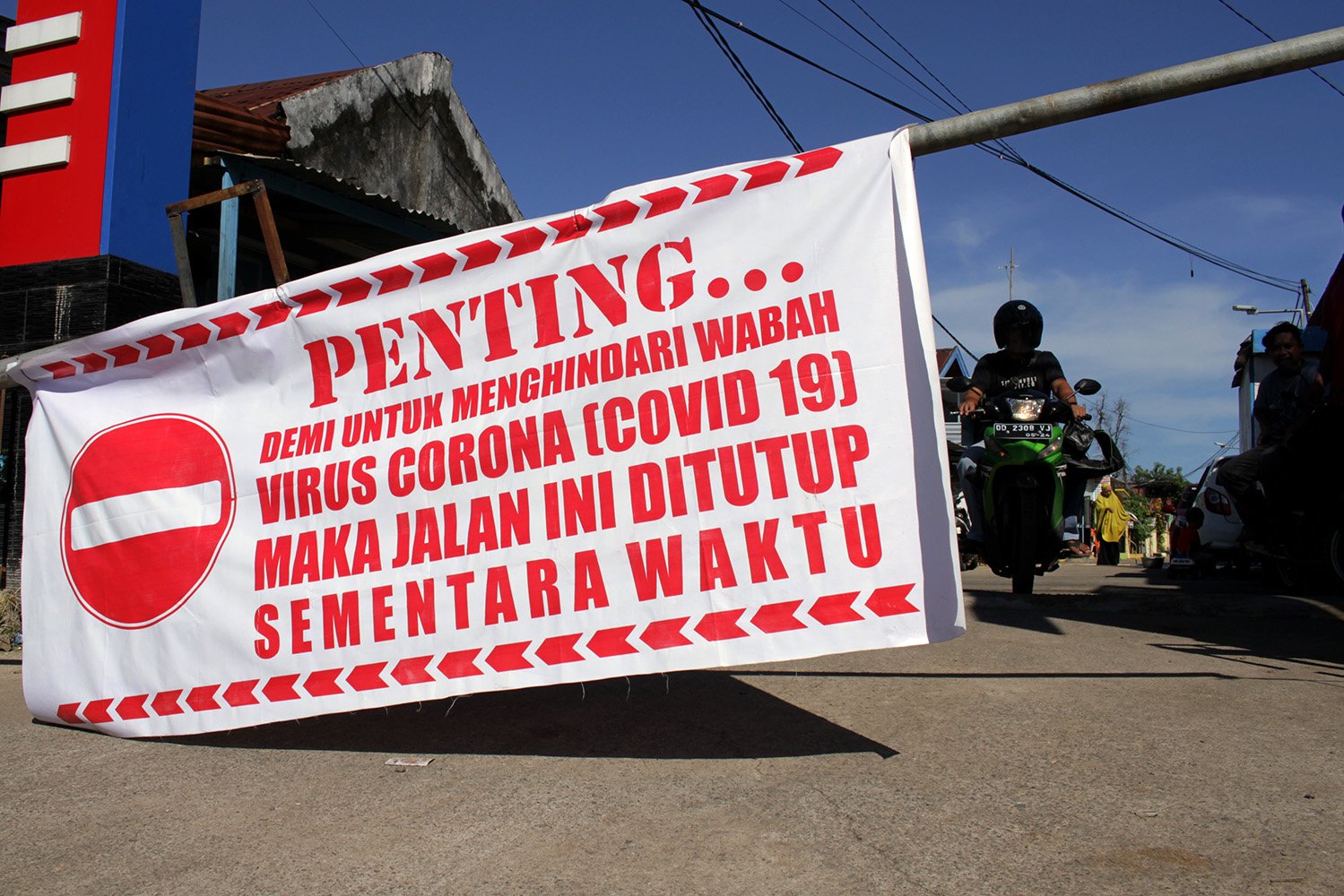 Warga melintas di dekat portal karantina wilayah di Makassar, Sulawesi Selatan. Warga setempat memberlakukan karantina wilayah secara mandiri dengan menutup akses jalan masuk permukiman bagi orang luar untuk mengurangi risiko penyebaran virus corona (Covid-19) di daerah itu. 
