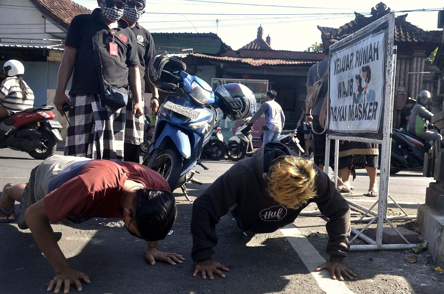 Pengendara yang tidak mengenakan masker melakukan \'push up\' saat diberikan sanksi oleh Pecalang atau petugas keamanan adat Bali dalam kegiatan sosialisasi dan edukasi pendisiplinan penggunaan masker di wilayah Desa Adat Intaran, Sanur, Denpasar.
