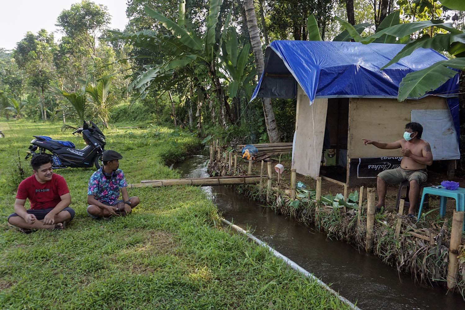 Wiranto (kanan) dengan masker di wajahnya berbincang bersama tetangganya dalam jarak aman di sekitar gubuk tempat isolasi mandirinya.