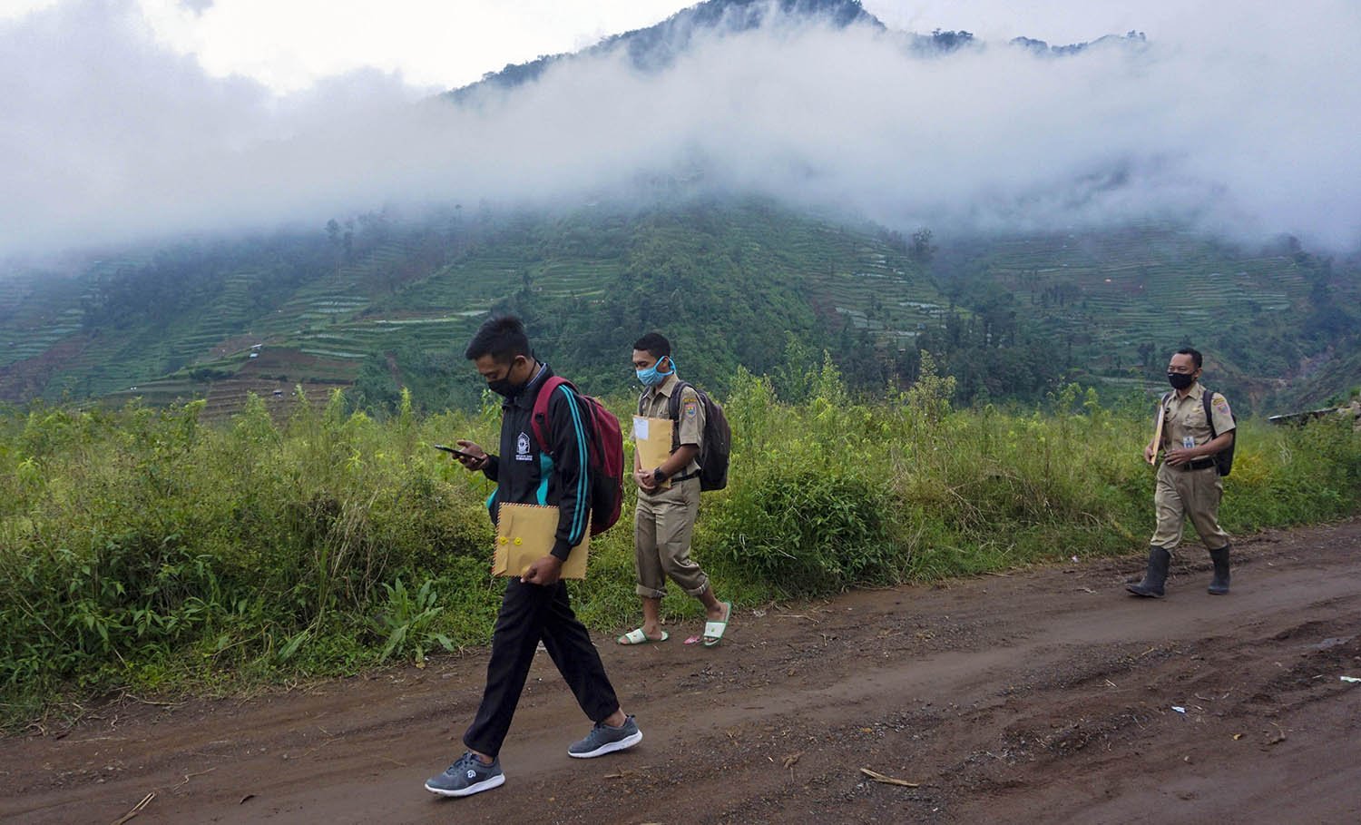 Kepala Sekolah SMP N 4 Bawang Mulud Sugito (kanan) dan guru Wiyata Bhakti berjalan kaki guna mengantar lembar tugas siswa langsung ke rumahnya di Pranten, Kecamatan Bawang, Kabupaten Batang, Jawa Tengah.
