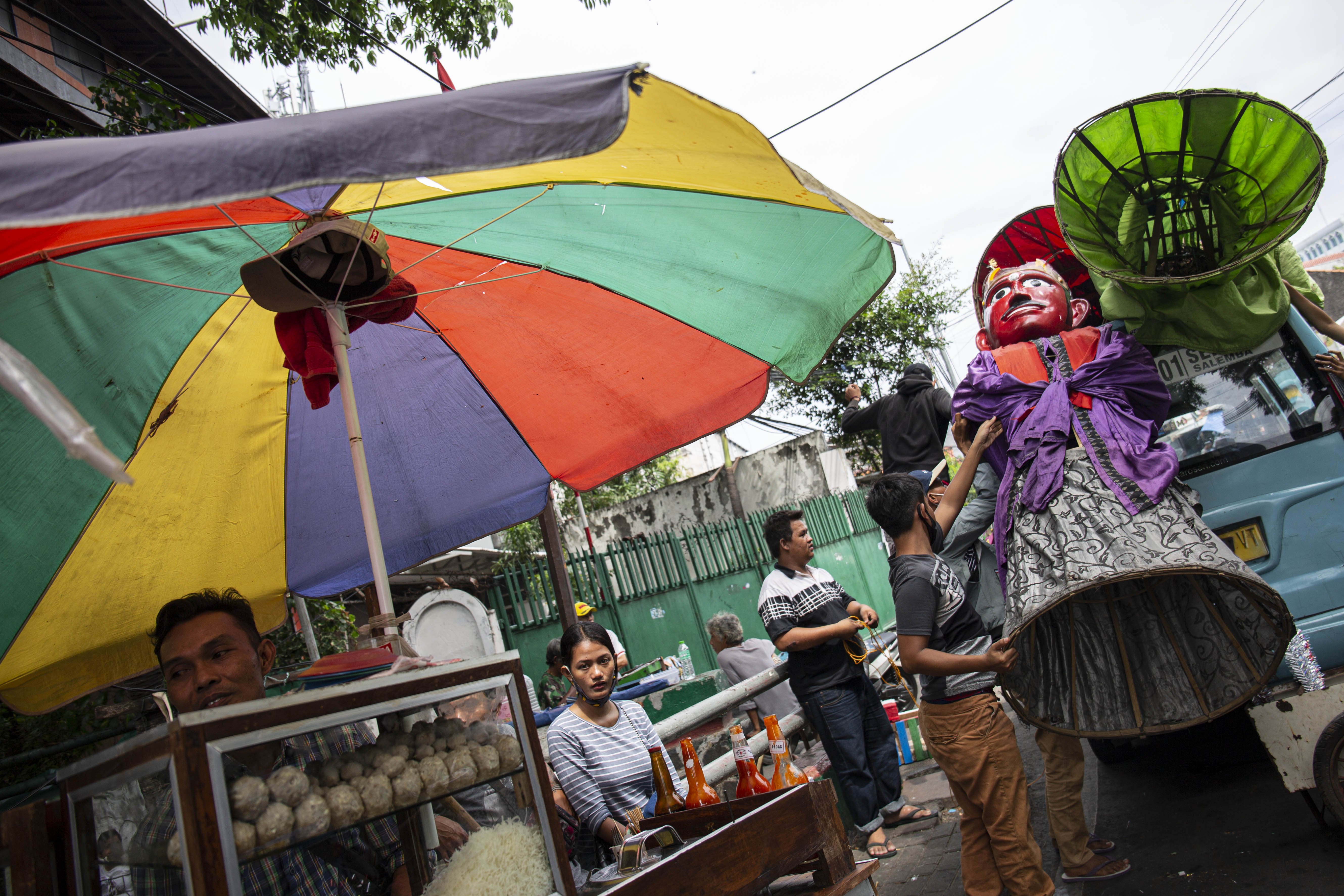 Pegiat seni jalanan menaikan boneka ondel-ondel keatas bajaj di Jalan Kembang Pacar, Kramat Pulo, Senen, Jakarta , Rabu (12/8/2020).