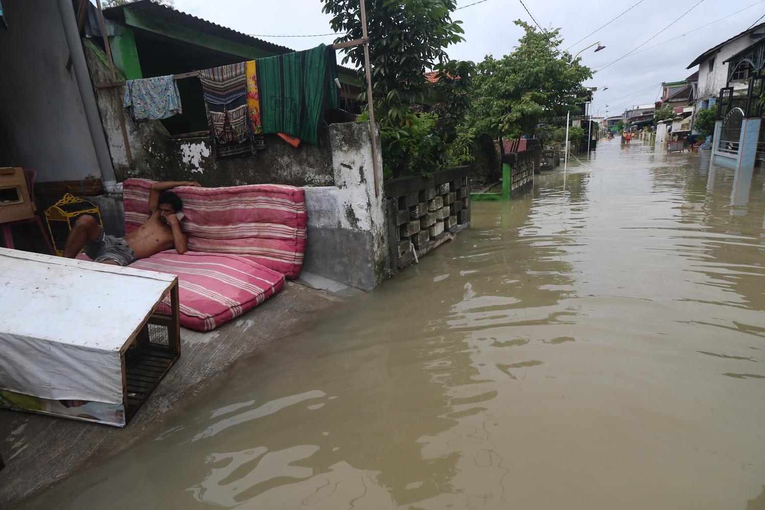 Warga duduk di samping jalan yang tergenang banjir di Dusun Nyanyat, Benjeng, Kabupaten Gresik, Jawa Timur, Senin (14/12/2020). Banjir itu akibat luapan Kali Lamong di Kabupaten Gresik, Jawa Timur.