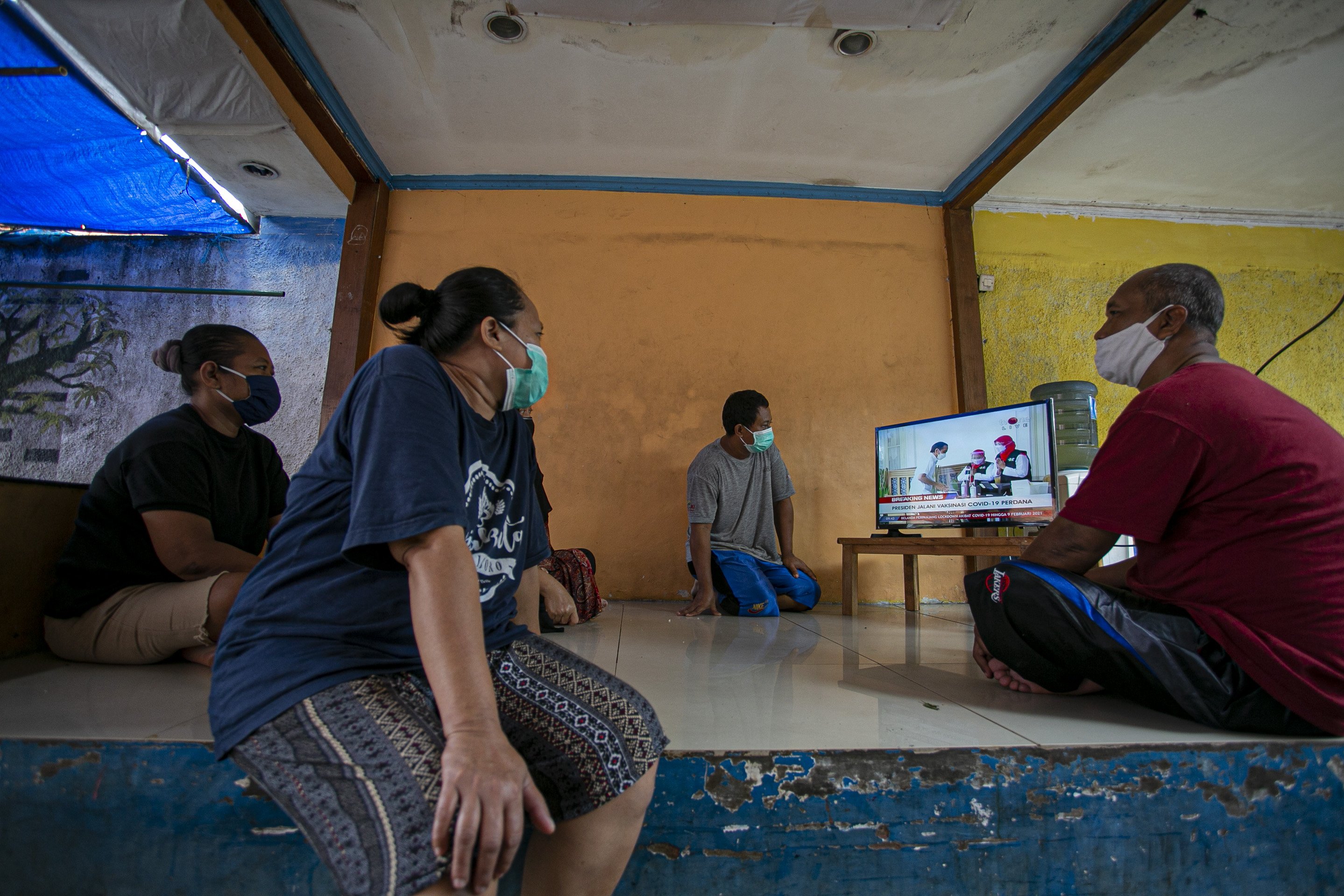 Warga menonton siaran langsung vaksinasi pertama kepada Presiden Indonesia Joko Widodo di kawasan Pejaten, Pasar Minggu, Jakarta Selatan, Rabu (13/1/2021).