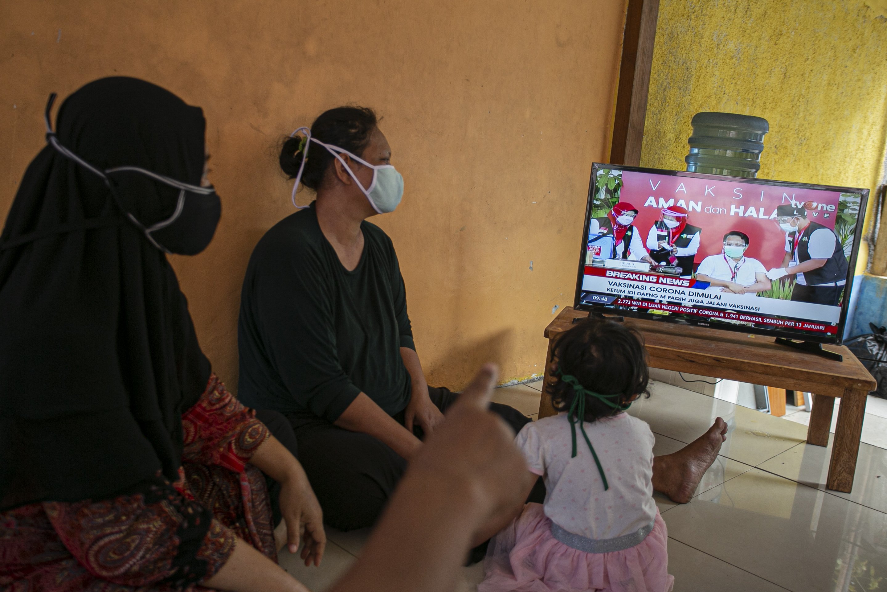 Warga menonton siaran langsung vaksinasi pertama di kawasan Pejaten, Pasar Minggu, Jakarta Selatan, Rabu (13/1/2021).