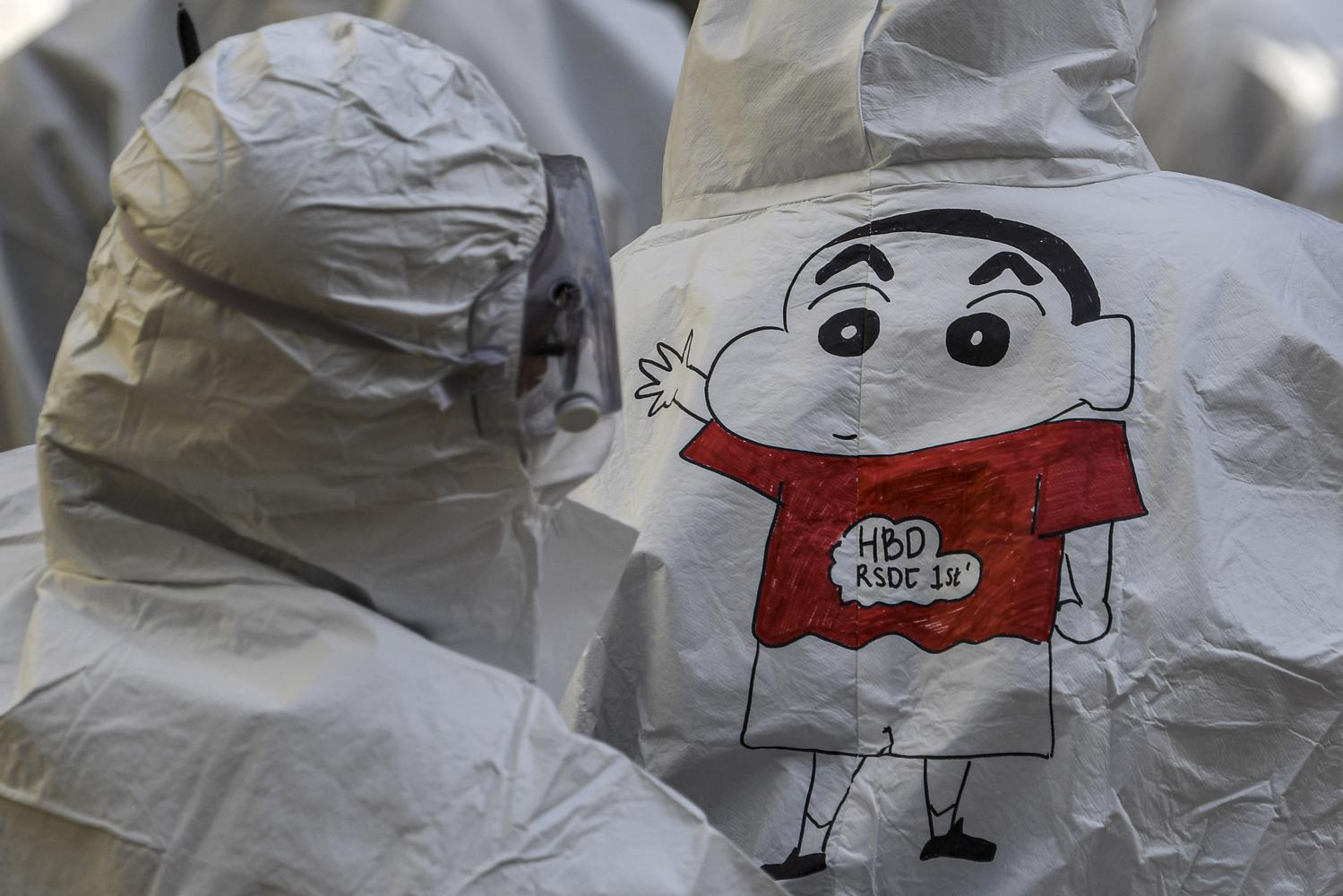 Seorang tenaga kesehatan melihat gambar karikatur Crayon Shinchan di hazmat rekannya saat peringatan satu tahun Rumah Sakit Darurat COVID-19 (RSDC) di Wisma Atlet, Kemayoran, Jakarta, Selasa (23/3/2021). Sebanyak 1.500 tenaga kesehatan bersama pasien COVID-19 memainkan angklung untuk memperingati satu tahun beroperasinya wisma atlet dalam penanganan pasien COVID-19.