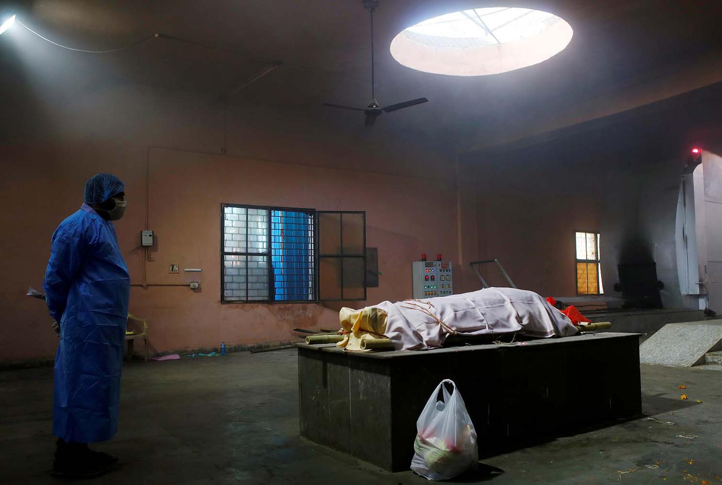 Adnan Abidi REFILE - CORRECTING INFORMATION Seorang anggota keluarga memakai alat pelindung diri (APD) di sebelah jenazah seorang wanita, yang meninggal akibat terinfeksi virus corona (COVID-19) sebelum dikremasi, di krematorium, New Delhi, India, Sabtu (24/4/2021).