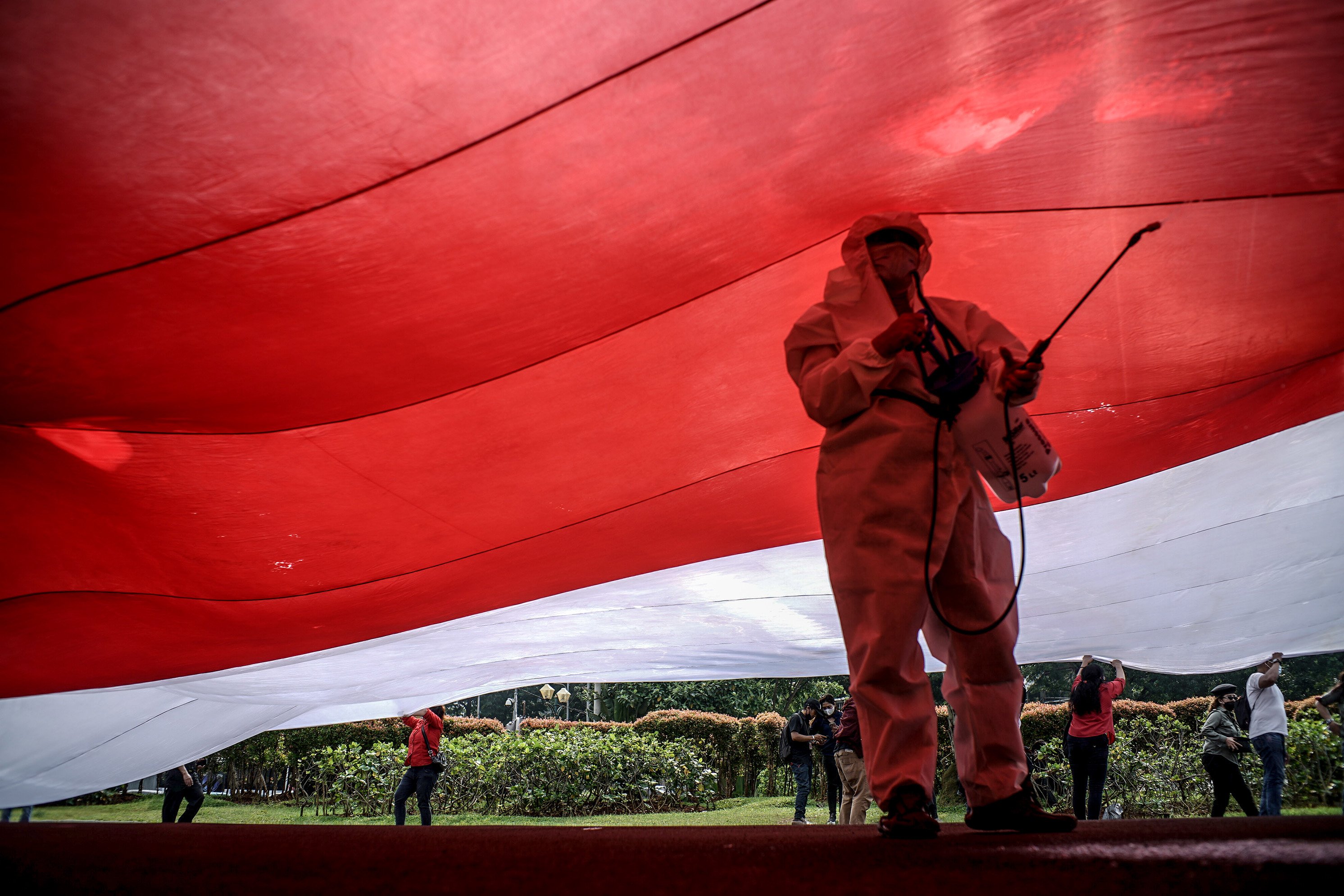 Sejumlah relawan yang tergabung dalam Gerakan Jaga Indonesia (GJI) menggunakan alat pelindung diri lengkap (APD) saat mengibarkan bendera merah putih raksasa di Patung Kuda, Jalan Merdeka Barat, Jakarta Pusat, Rabu (2/6/2021). Pengibaran bendera merah putih raksasa tersebut dilakukan masa aksi dalam memperingati hari lahir pancasila.