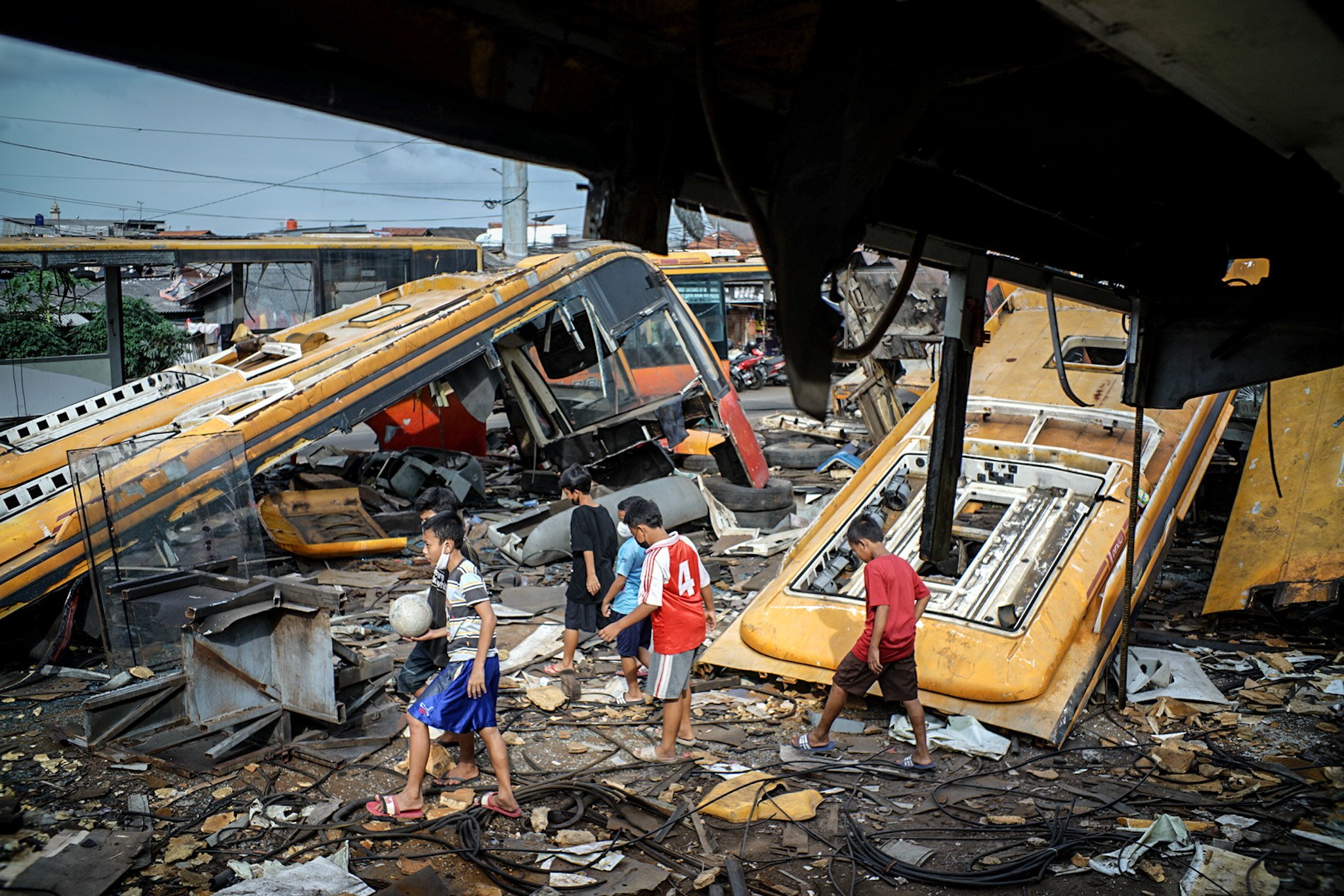 Sejumlah bocah melintas di area bangkai bus Transjakarta di Terminal Polugadung, Jakarta Timur, Kamis, (24/6/2021). Lebih dari lima puluh bus Transjakarta terbengkalai dan potongan dari bangkai bus tersebut dimanfaatkan oleh warga setempat untuk dijual kembali dengan harga jual Rp. 4.000 per kilogram.