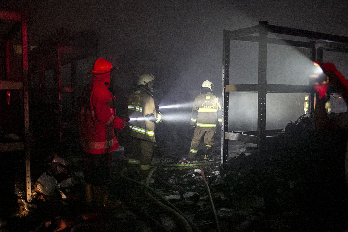 Suku Dinas Penanggulangan Kebakaran dan Penyelamatan (Gulkarmat) mengamati area gudang menggunakan senter usai memadamkan kobaran api yang melahap gudang farmasi di kawasan Cipinang Muara 2, Duren Sawit, Jakarta Timur, Kamis, (8/7/2021). Sebanyak 12 mobil pemadam dan 60 personel dikerahkan untuk memamdamkan kebakaran tersebut.