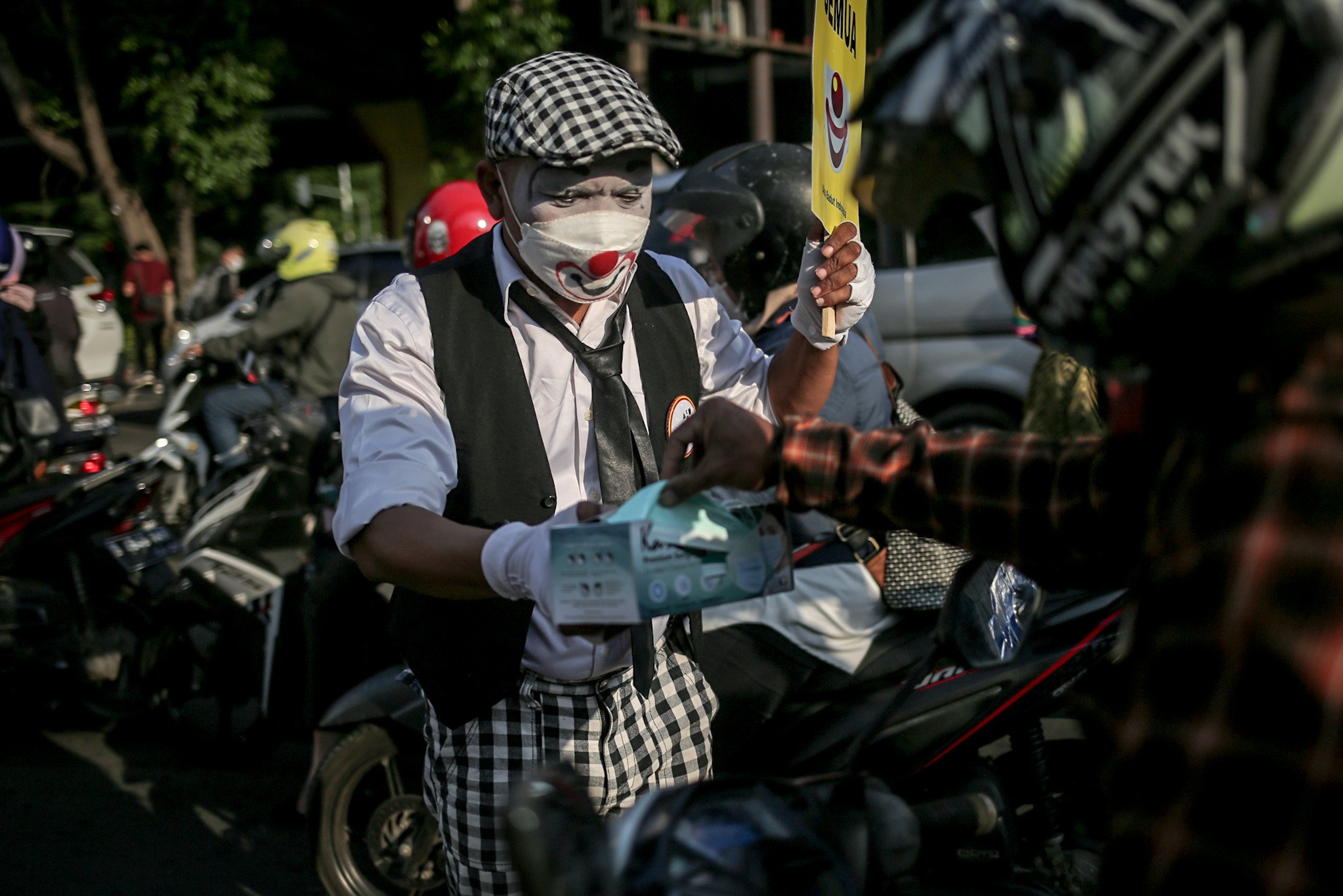 Anggota komunitas Aku Badut Indonesia (ABI) mensosialisasikan dan membagikan masker medis bagi pengendara untuk menggunakan masker dua lapis selama masa Pemberlakuan Pembatasan Kegiatan Masyarakat (PPKM) di ruas Jalan TB. Simatupang, Fatmawati, Cilandak Barat, Jakarta Selatan, Senin, (12/7/2021). Langkah tersebut dilakukan untuk mencegah kemungkinan terpapar virus varian baru di tegah lonjakan kasus Covid-19 di Jakarta.