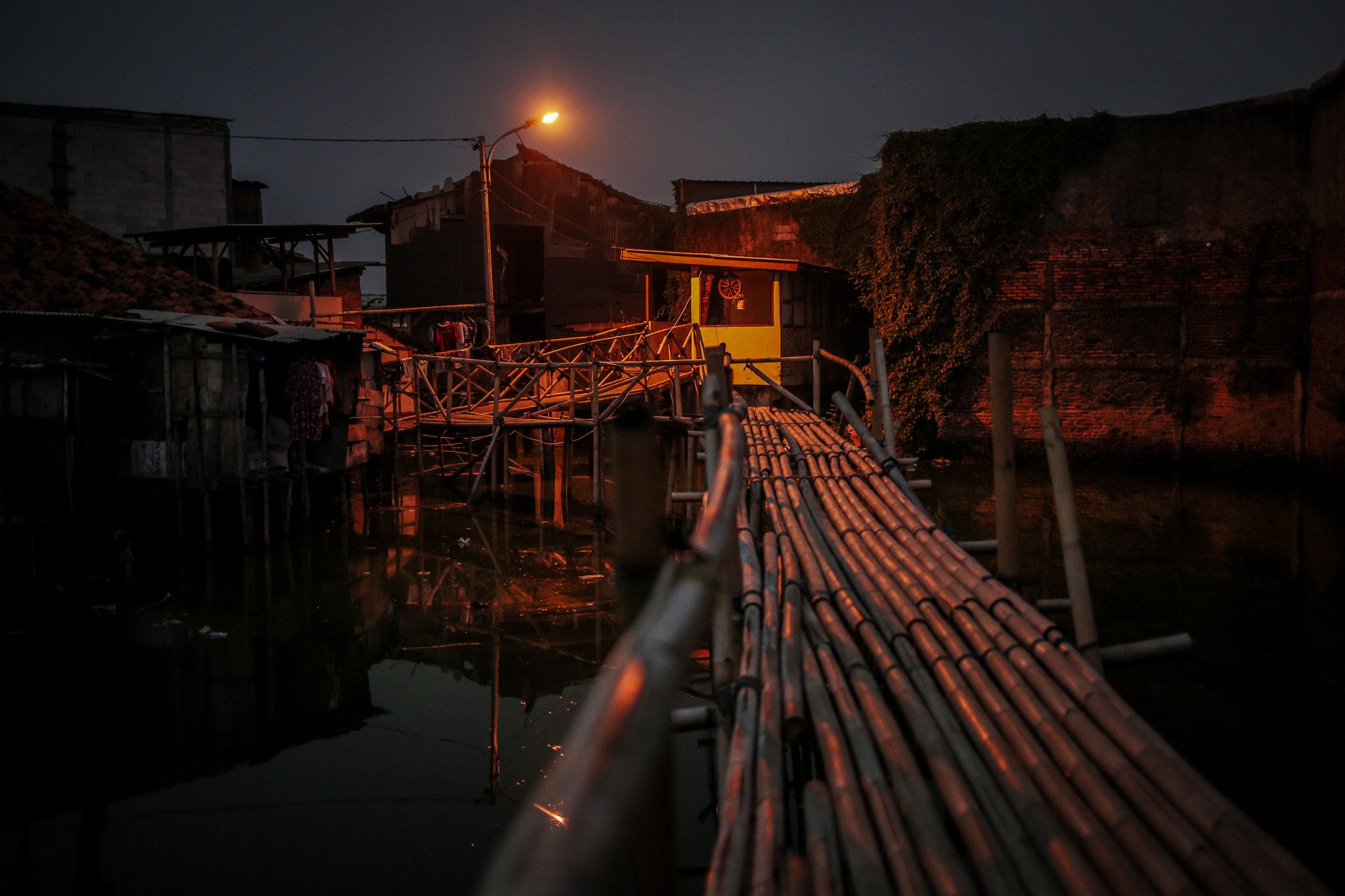Jembatan penyebrangan orang yang terbuat dari bambu menjadi akses pejalan kaki yang hendak menyebrang di Kampung Apung, Kapuk, Cengkareng, jakarta, Kamis, (29/7/2021).