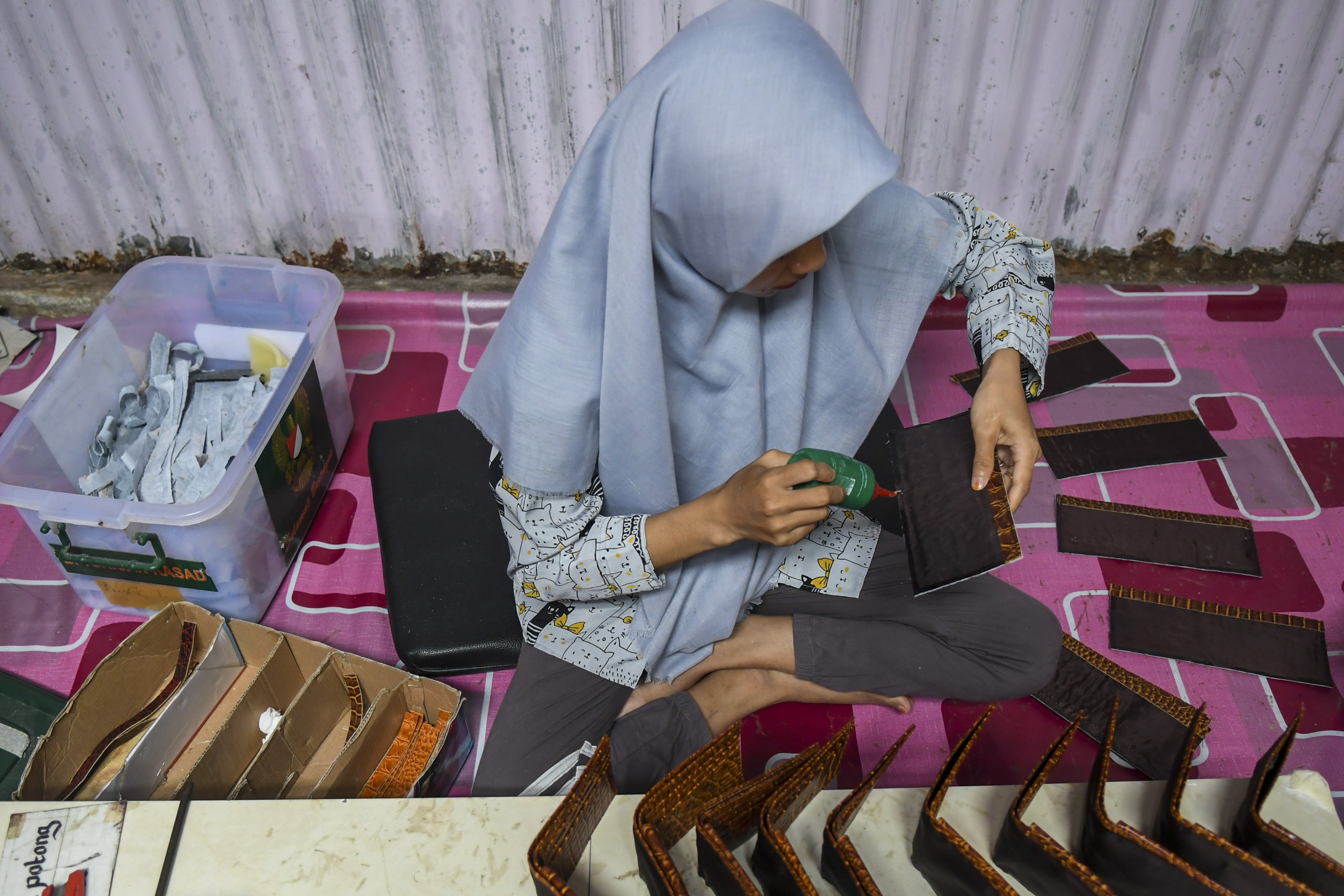 Pekerja meberi perekat pada dompet berbahan dasar kulit buaya saat proses penyelesaian kerjinan tangan ari kulit buaya di Merauke, Papua.