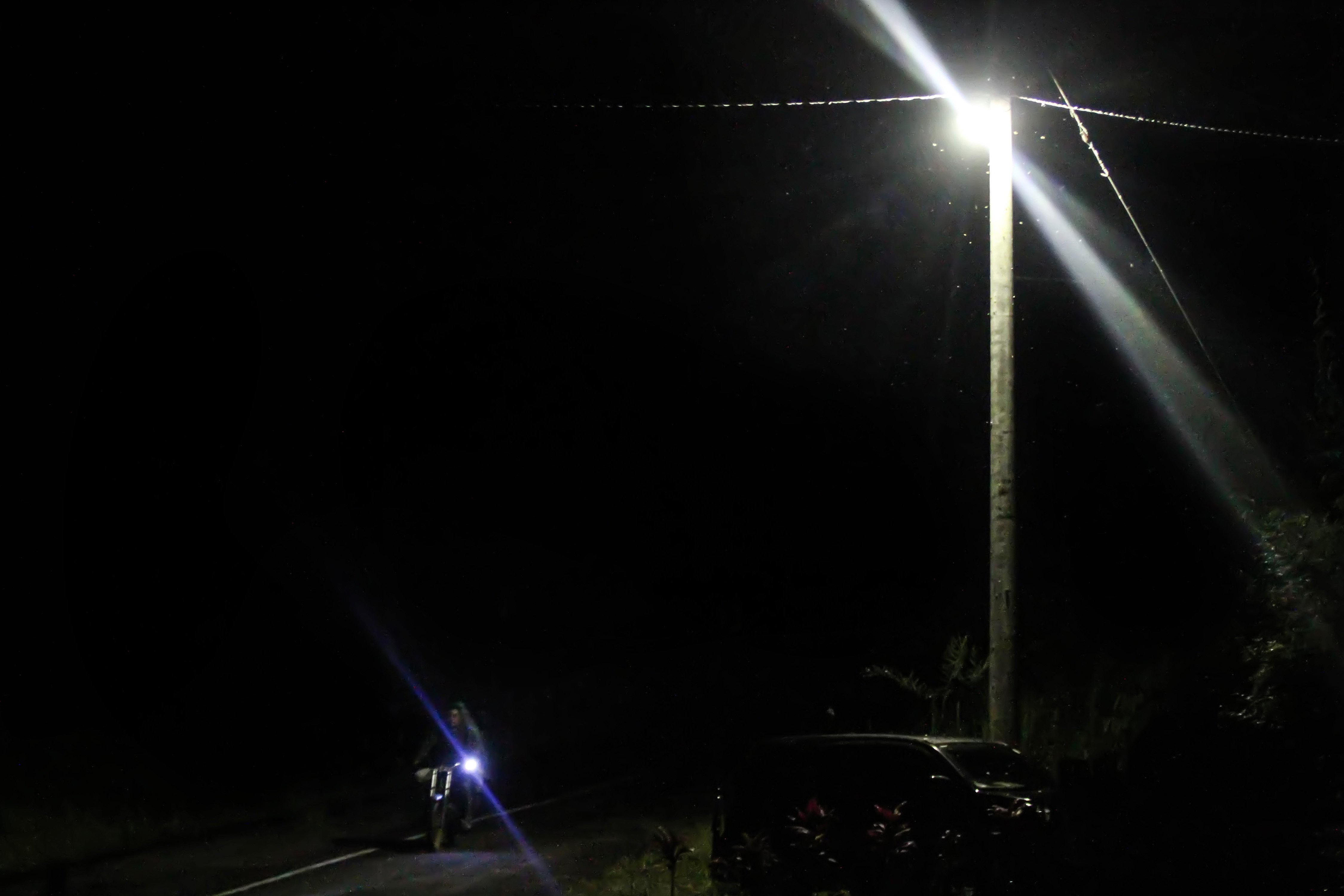 Seorang pengendara sepeda motor melintas di jalan raya yang tersorot sinar lampu yang tersalur dengan jaringan listrik melalui program listrik masuk wilayah desa tertinggal di Dusun Jabal Antara, Aceh Utara.