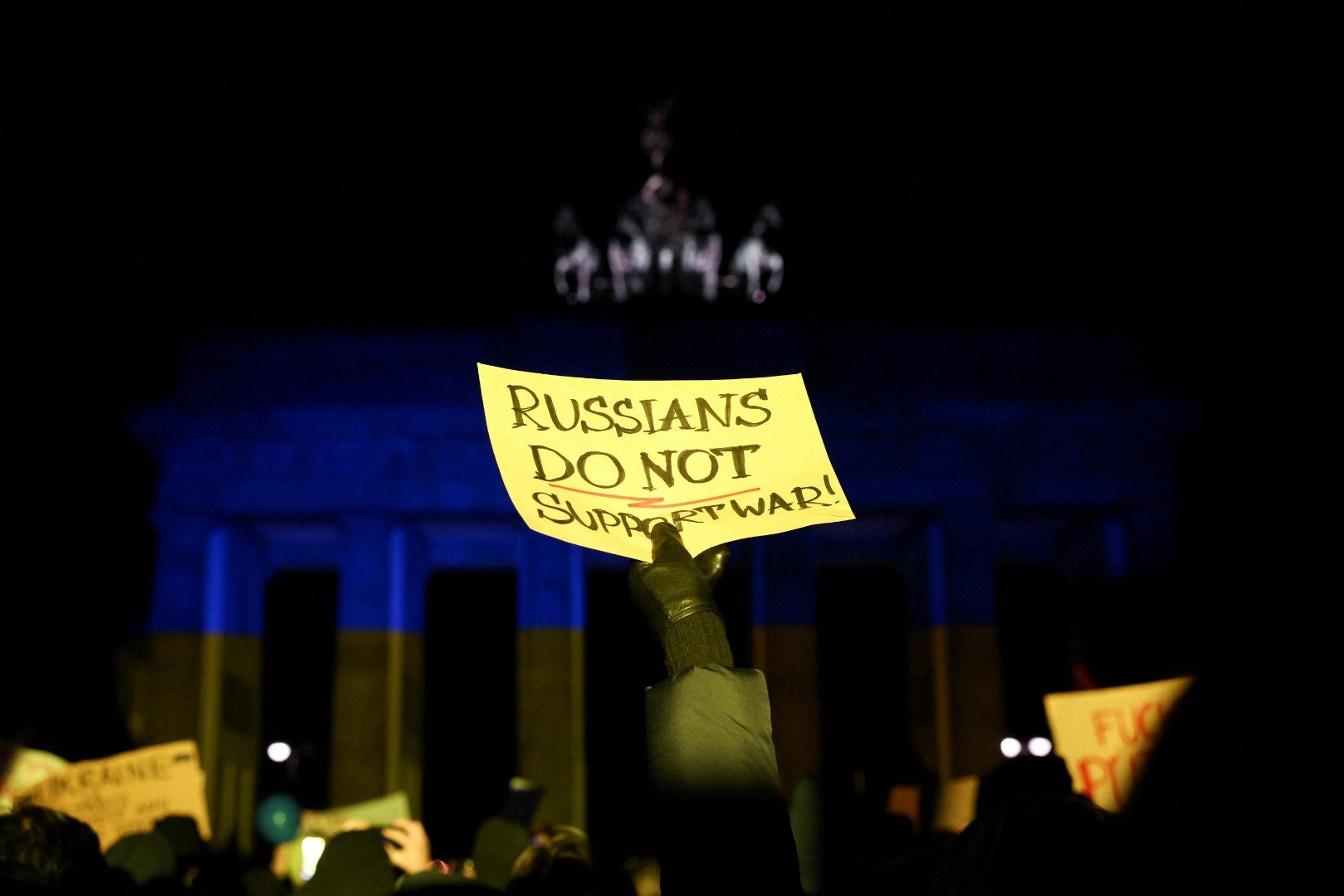 Seorang warga membawa poster di depan Brandenburg Gate yang menyala dengan lampu warna bendera Ukraina saat protes anti perang, setelah Rusia meluncurkan operasi militer besar terhadap Ukraina, di Berlin, Jerman, Kamis (24/2/2022). ANTARA FOTO/REUTERS/Christian Mang/hp/cfo\r\n