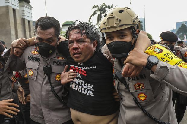 Dua orang personel kepolisian memapah penggiat Media Sosial Ade Armando (tengah) yang terluka akibat dianiaya massa di lokasi unjuk rasa, di depan Kompleks Parlemen, Senayan, Jakarta, Senin (11/4/2022).
