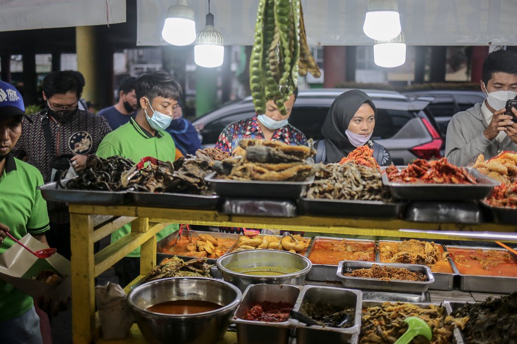 Pelayan melayani pembeli yang mengantre saat membeli menu berbuka puasa di Sentra kuliner Nasi Kapau di Jalan Kramat Raya, Senen, Jakarta Pusat, Selasa (12/4/2021). Menjelang berbuka puasa sentra kuliner yang menyajikan makanan khas sumatra barat ini selalu ramai dikunjungi pembeli.