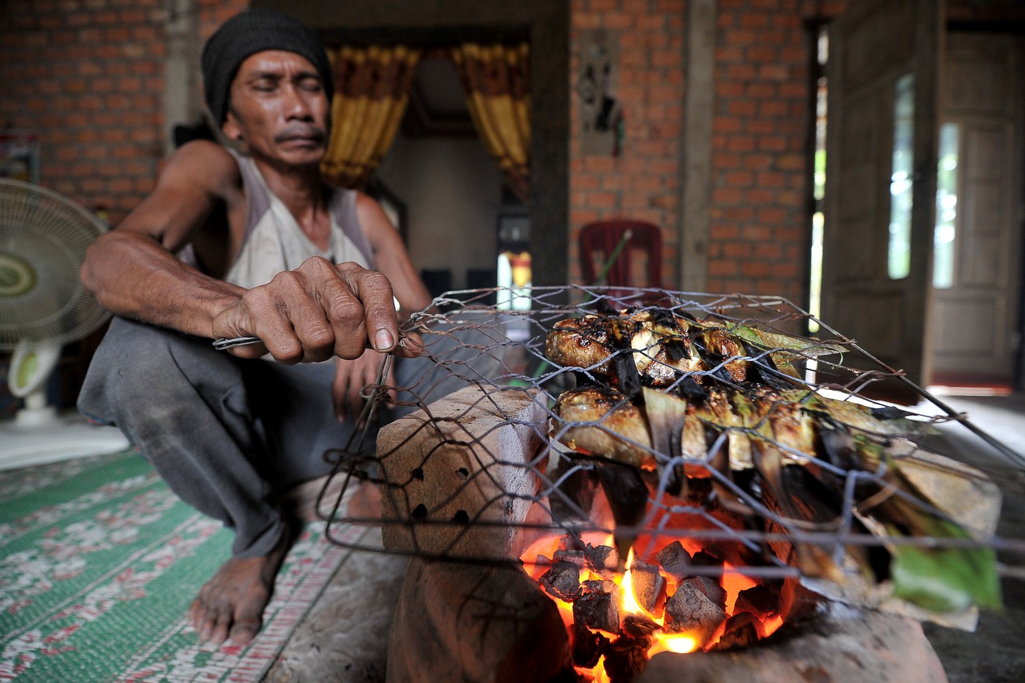 Guntoro membakar ikan menggunakan briket buatannya di rumahnya.