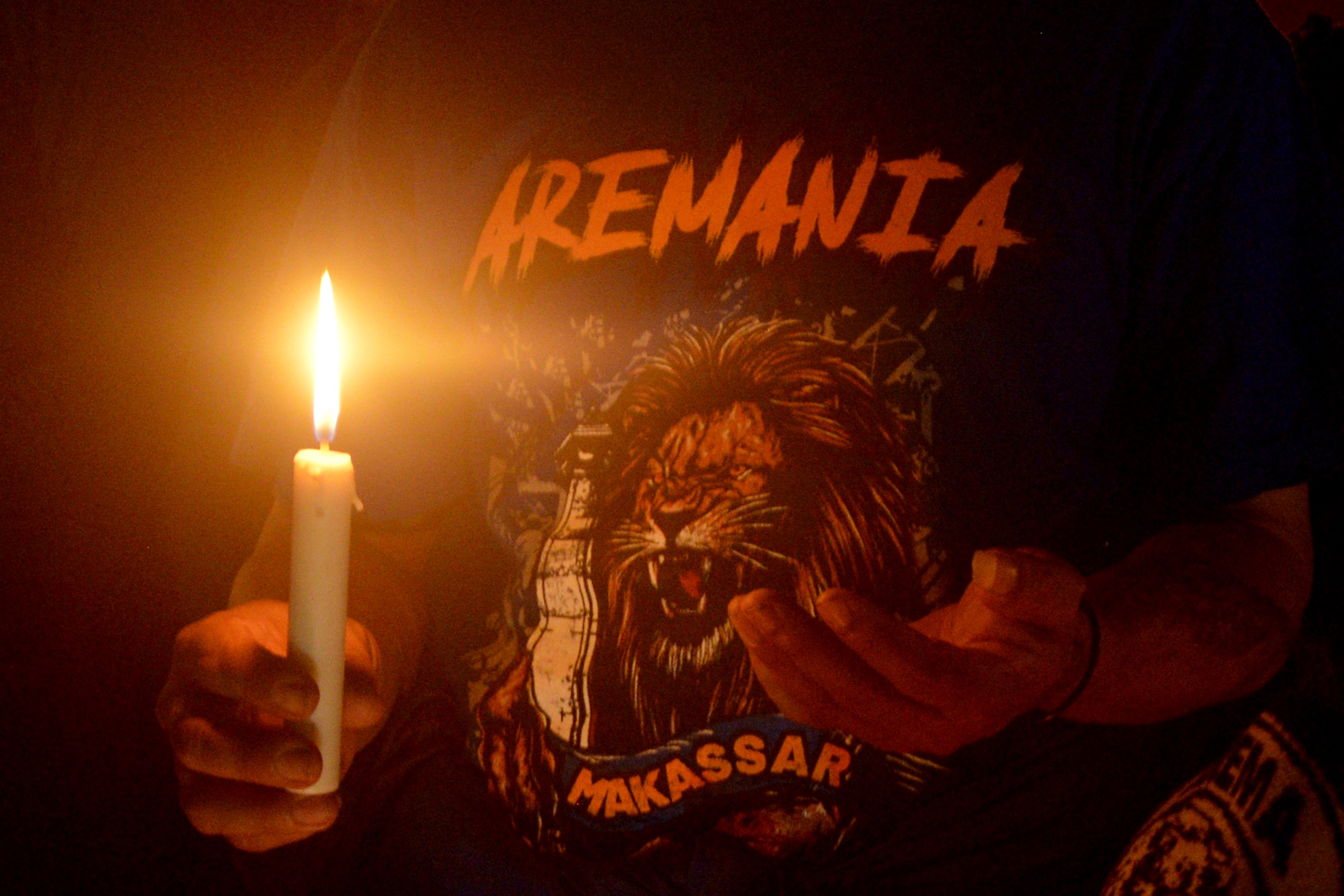 Seorang suporter Aremania berdoa saat melakukan aksi menyalakan lilin di depan Monumen Mandala, Makassar, Sulawesi Selatan, Minggu (2/10/2022) malam. Aksi tersebut sebagai bentuk solidaritas dan doa bersama untuk para suporter Arema yang menjadi korban kerusuhan di Stadion Kanjuruhan seusai pertandingan Liga I Arema FC melawan Persebaya. ANTARA FOTO/Abriawan Abhe/nym.