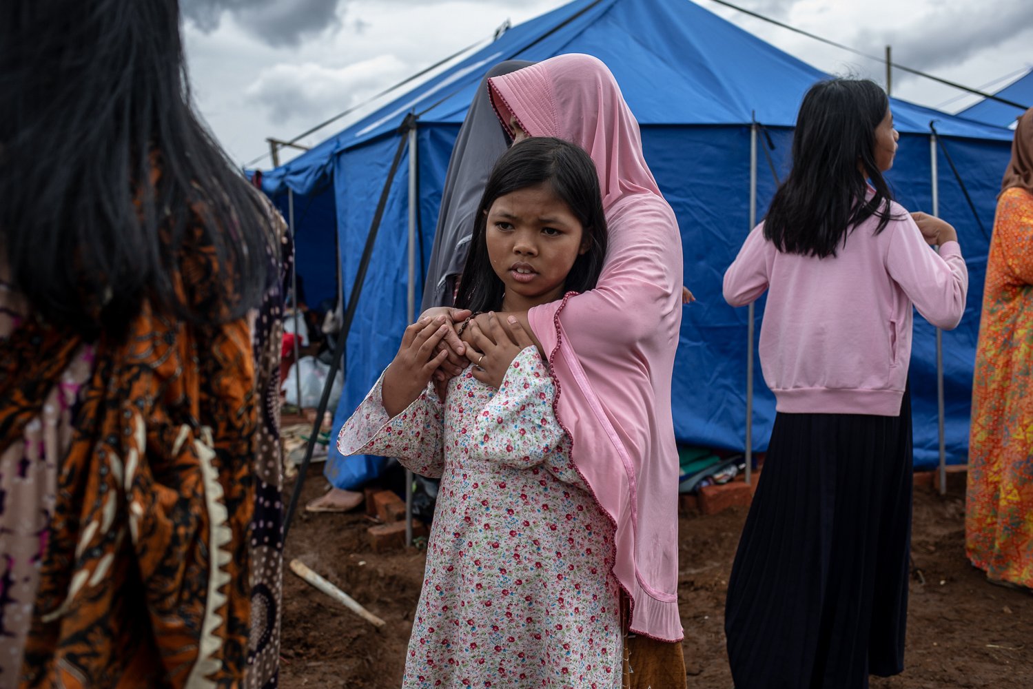 Seorang ibu memeluk anaknya saat diterpa angin kencang di tenda pengungsian pasca gempa bumi dengan magnitude 5.6 di Desa Mangunkerta, Cugenang, Cianjur, Jawa Barat, Sabtu (26/11). Badan Nasional Penanggulangan Bencana (BNPB) mencatat total 321 orang meninggal dunia, jumlah pengungsi hingga hari ini mencapai 73.874 orang akibat gempa di Cianjur.
