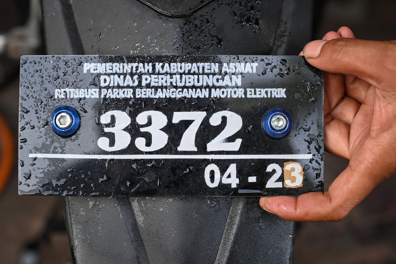 Warga pemilik sepeda motor listrik menunjukkan pelat tanda telah membayar retribusi kepada pemerintah daerah setempat yang diperbarui setahun sekali di Agats, Kabupaten Asmat, Papua Selatan.