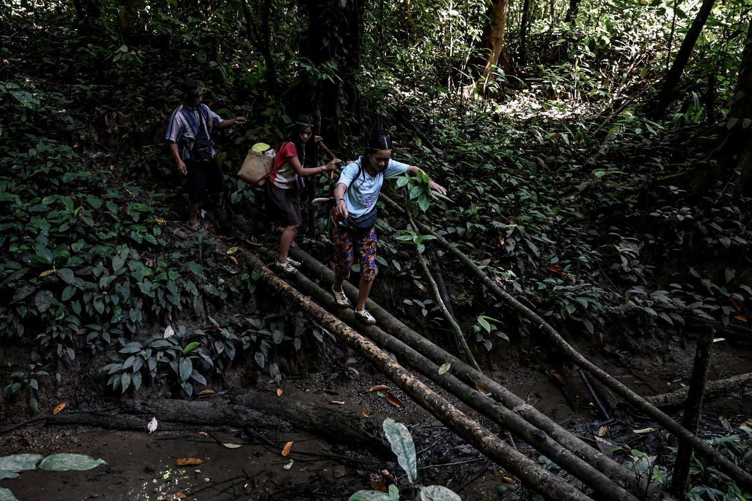 Ngakokup (kanan), Manik (kiri), dan Siti (tengah) menyebrangi jembatan kayu di tengah hutan saat berburu.