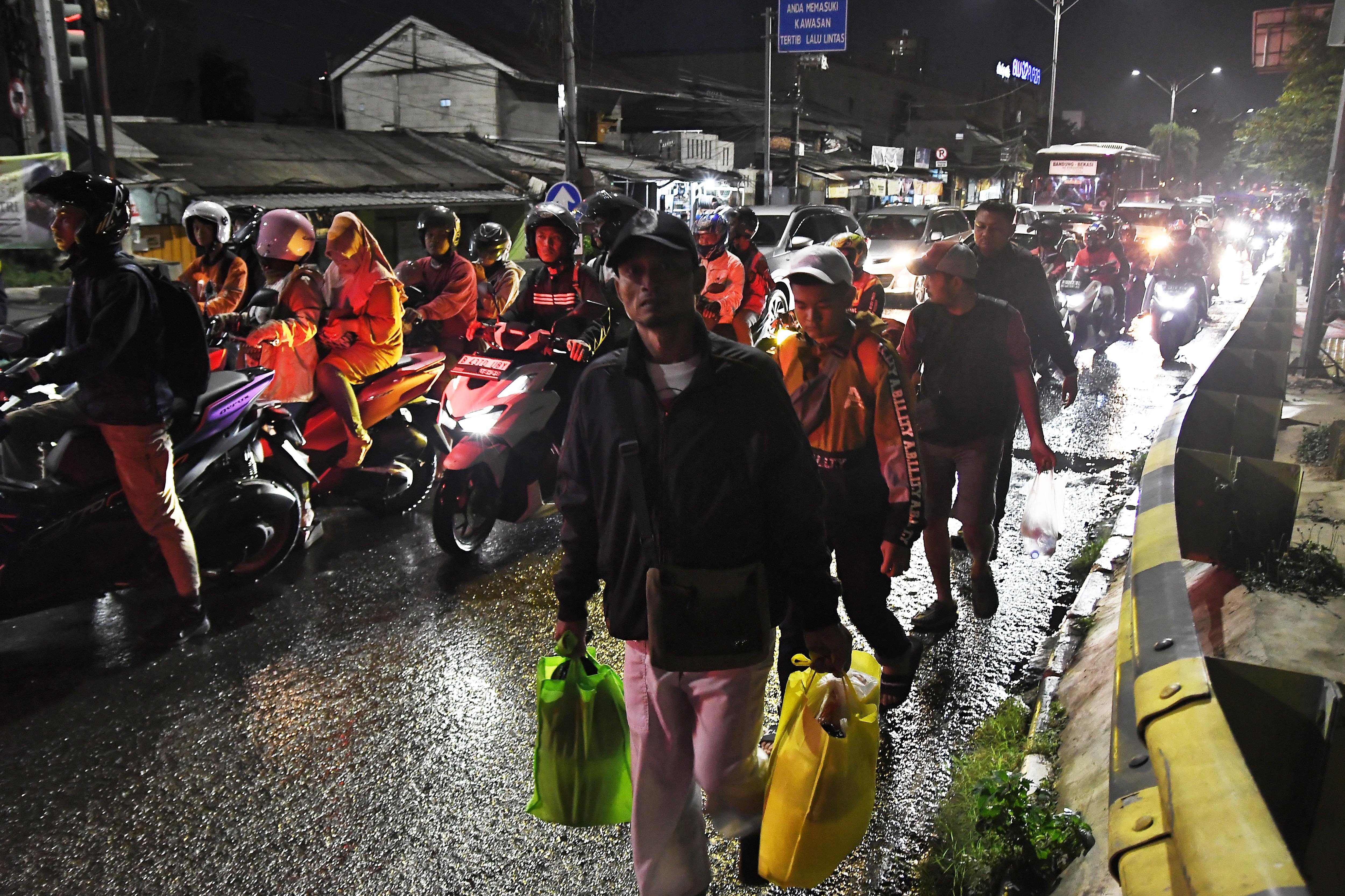 Sejumlah pemudik berjalan kaki usai turun dari bus di Jalan Chairil Anwar, Bekasi, Jawa Barat, Minggu (14/4/2024). Pada H+4 lebaran jalan tersebut dipadati pemudik yang menggunakan sepeda motor dan bus yang menurunkan penumpang di pinggir jalan. 