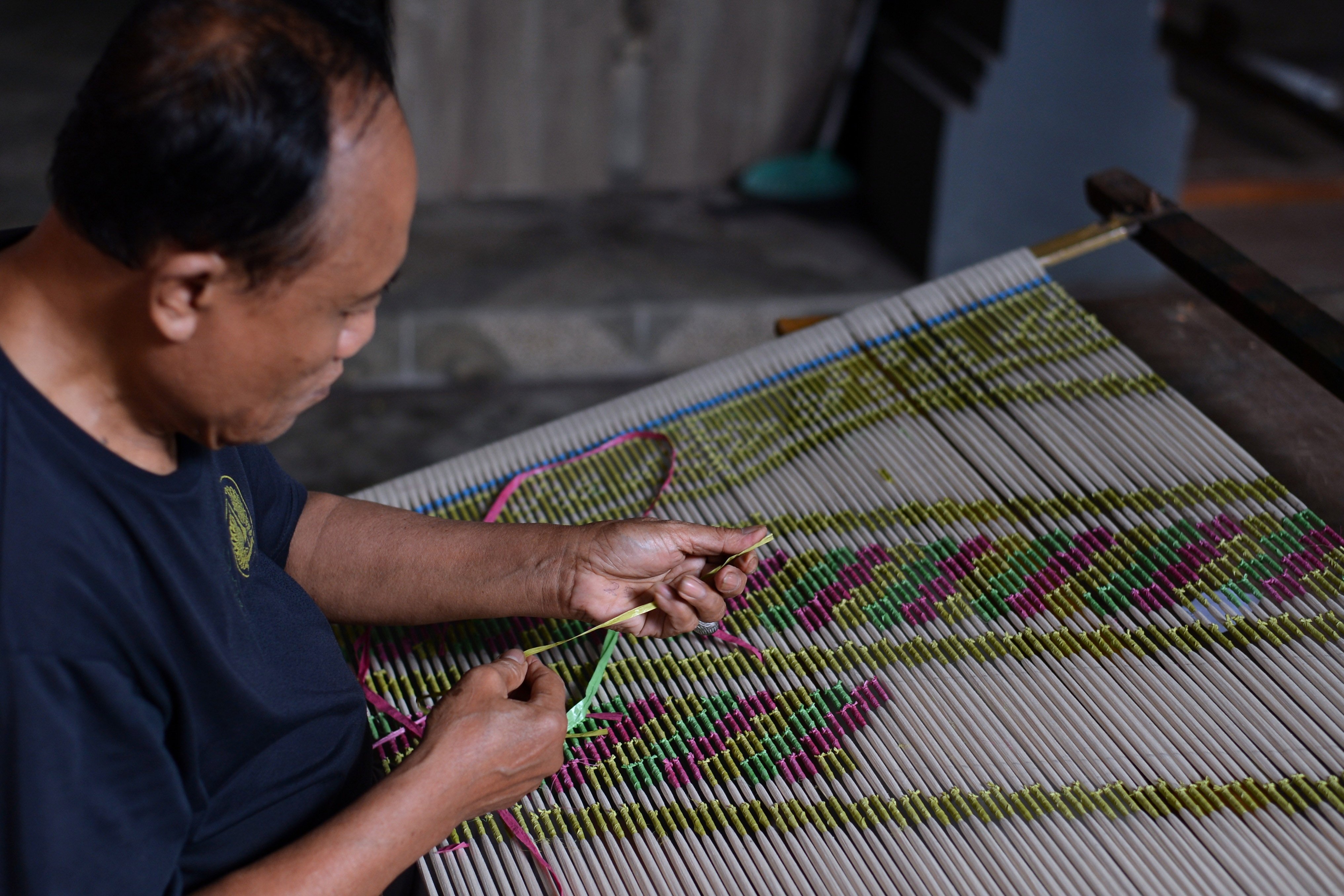 Pekerja mengikat benang membentuk motif kain endek sebelum proses pewarnaan di Gianyar, Bali.