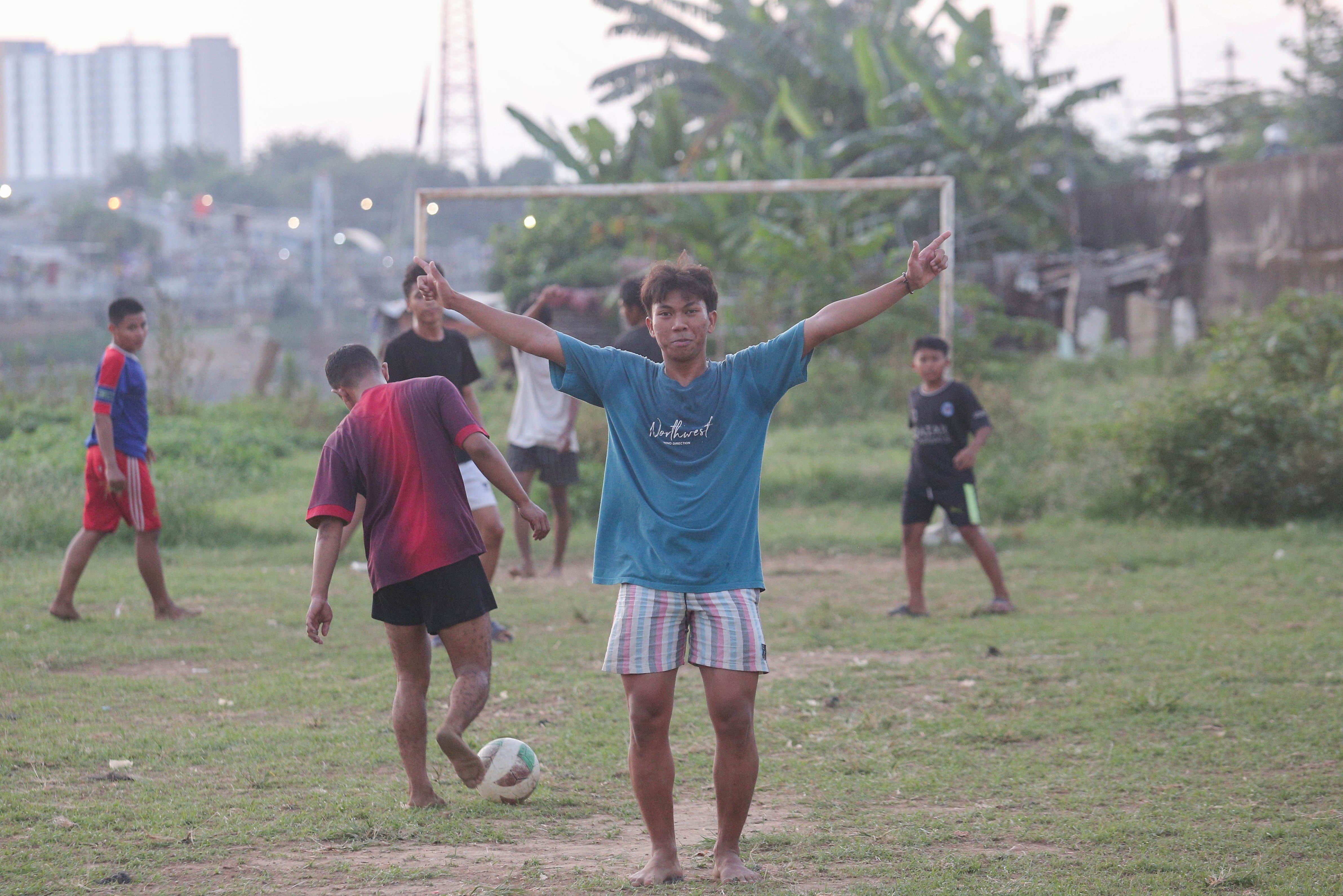 Seorang warga berselebrasi setelah mencetak gol saat saat bermain sepak bola di bantaran Kali Ciliwung di Jalan Setia Kawan III, Duri Pulo, Jakarta Pusat, Selasa (16/7/2024). Terbatasnya ruang terbuka hijau (RTH) di sekitar wilayah tersebut membuat warga memanfaatkan lahan kosong di bantaran kali untuk bermain sepak bola.