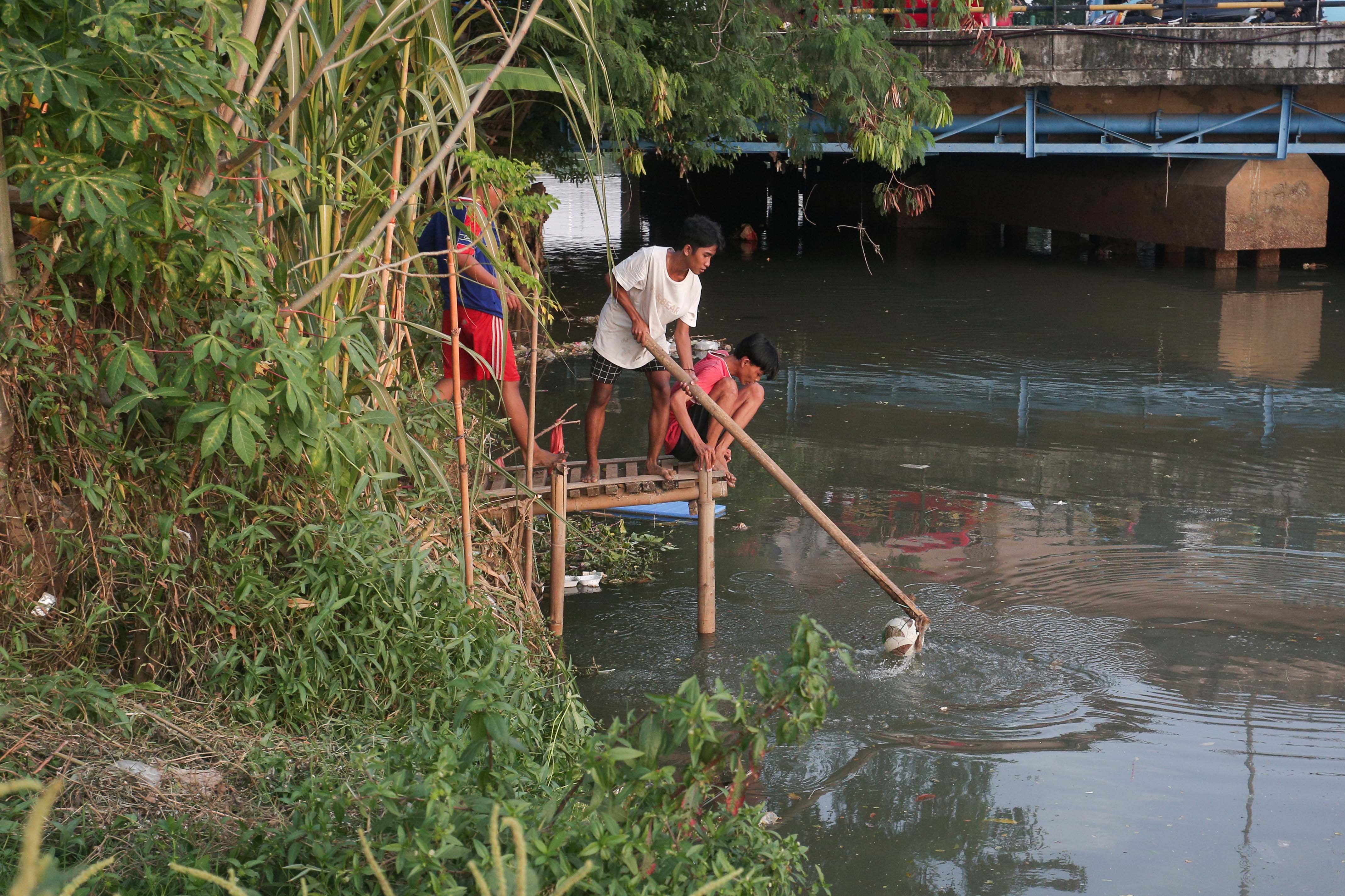 Warga berusaha mengambil bola yang tercebur ke kali saat bermain sepak bola di bantaran Kali Ciliwung di Jalan Setia Kawan III, Duri Pulo, Jakarta Pusat, Selasa (16/7/2024). Terbatasnya ruang terbuka hijau (RTH) di sekitar wilayah tersebut membuat warga memanfaatkan lahan kosong di bantaran kali untuk bermain sepak bola.