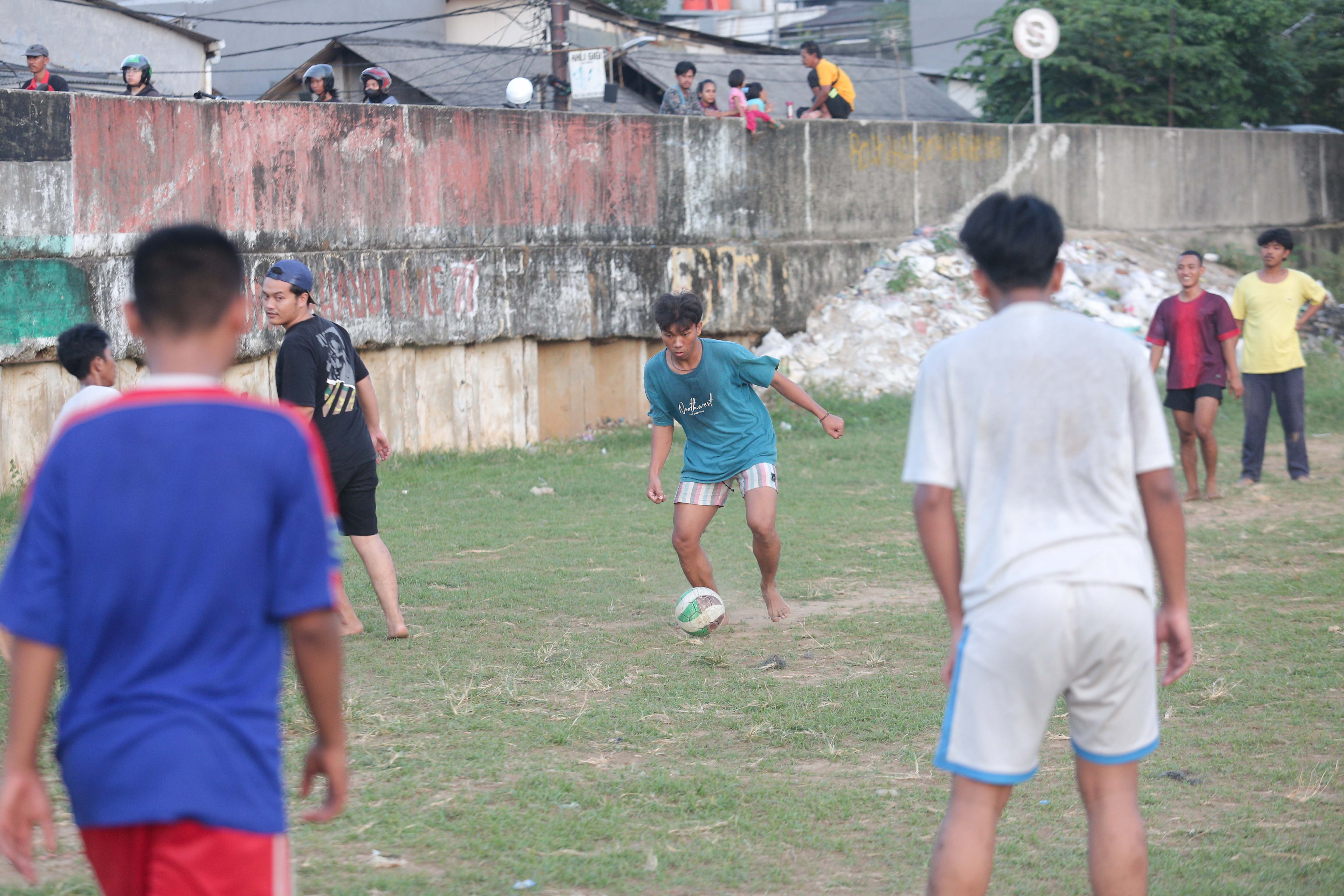 Sejumlah warga bermain sepak bola di bantaran Kali Ciliwung di Jalan Setia Kawan III, Duri Pulo, Jakarta Pusat, Selasa (16/7/2024). Terbatasnya ruang terbuka hijau (RTH) di sekitar wilayah tersebut membuat warga memanfaatkan lahan kosong di bantaran kali untuk bermain sepak bola.