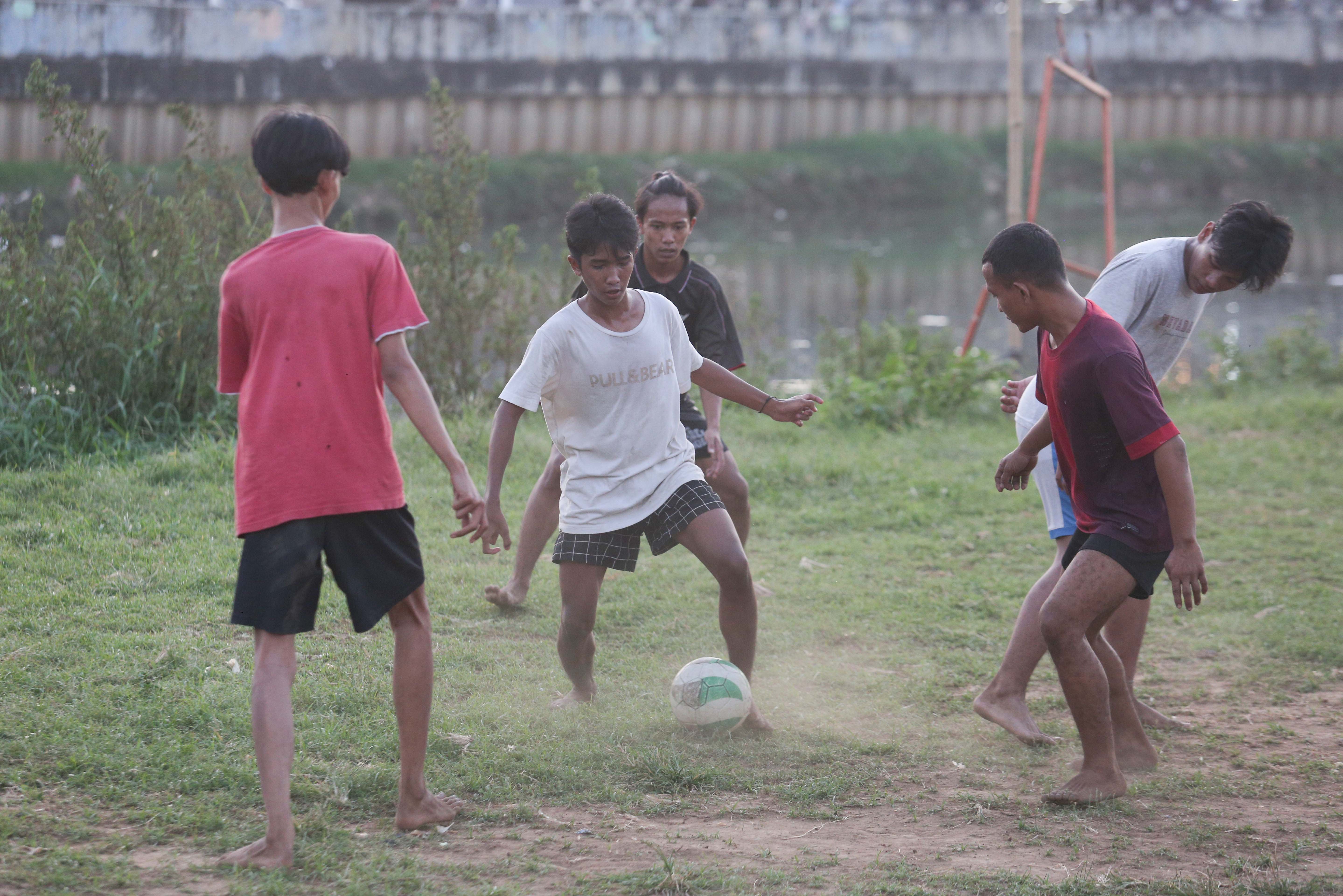 Sejumlah warga bermain sepak bola di bantaran Kali Ciliwung di Jalan Setia Kawan III, Duri Pulo, Jakarta Pusat, Selasa (16/7/2024). Terbatasnya ruang terbuka hijau (RTH) di sekitar wilayah tersebut membuat warga memanfaatkan lahan kosong di bantaran kali untuk bermain sepak bola.