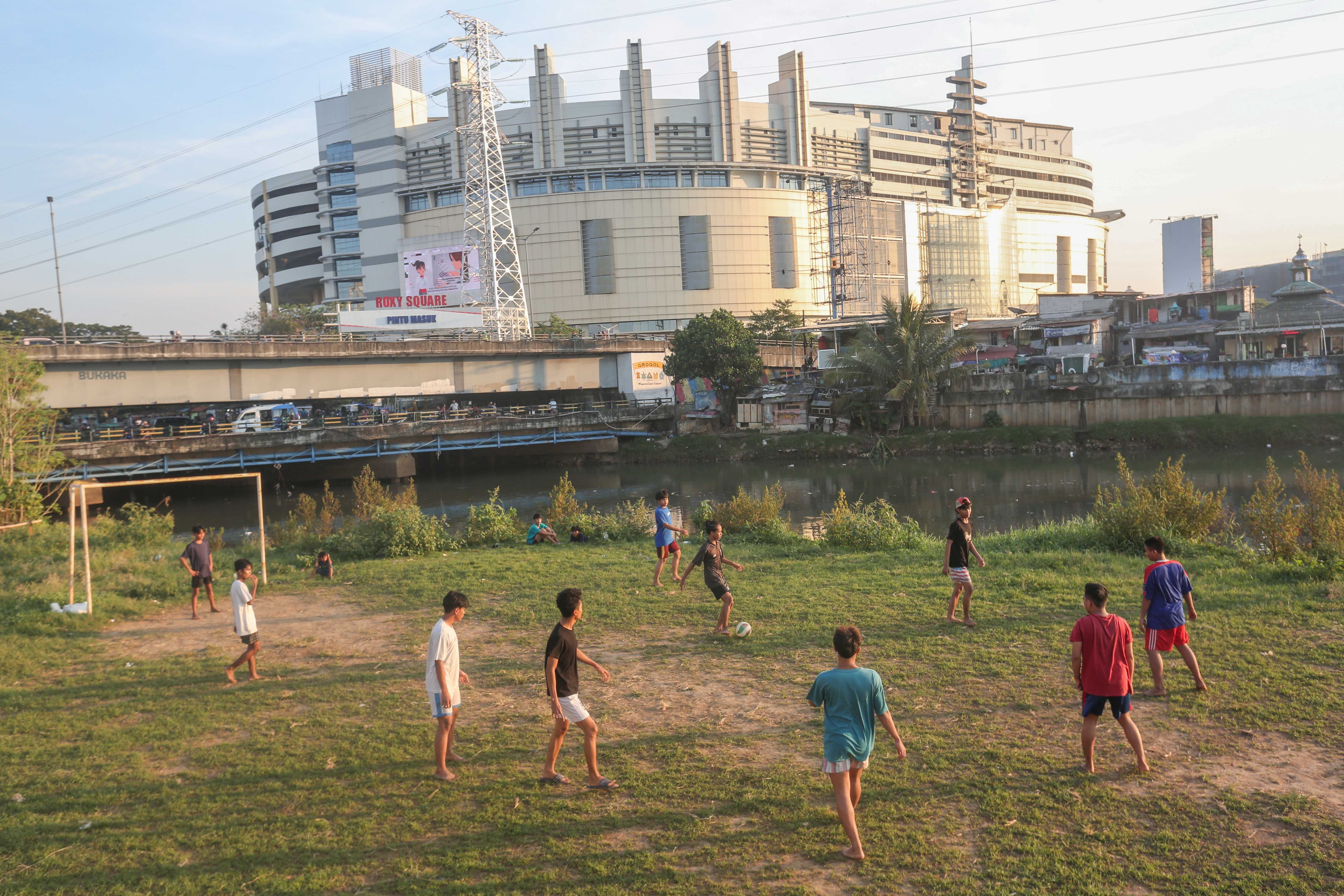 Sejumlah warga bermain sepak bola di bantaran Kali Ciliwung di Jalan Setia Kawan III, Duri Pulo, Jakarta Pusat, Selasa (16/7/2024). Terbatasnya ruang terbuka hijau (RTH) di sekitar wilayah tersebut membuat warga memanfaatkan lahan kosong di bantaran kali untuk bermain sepak bola.