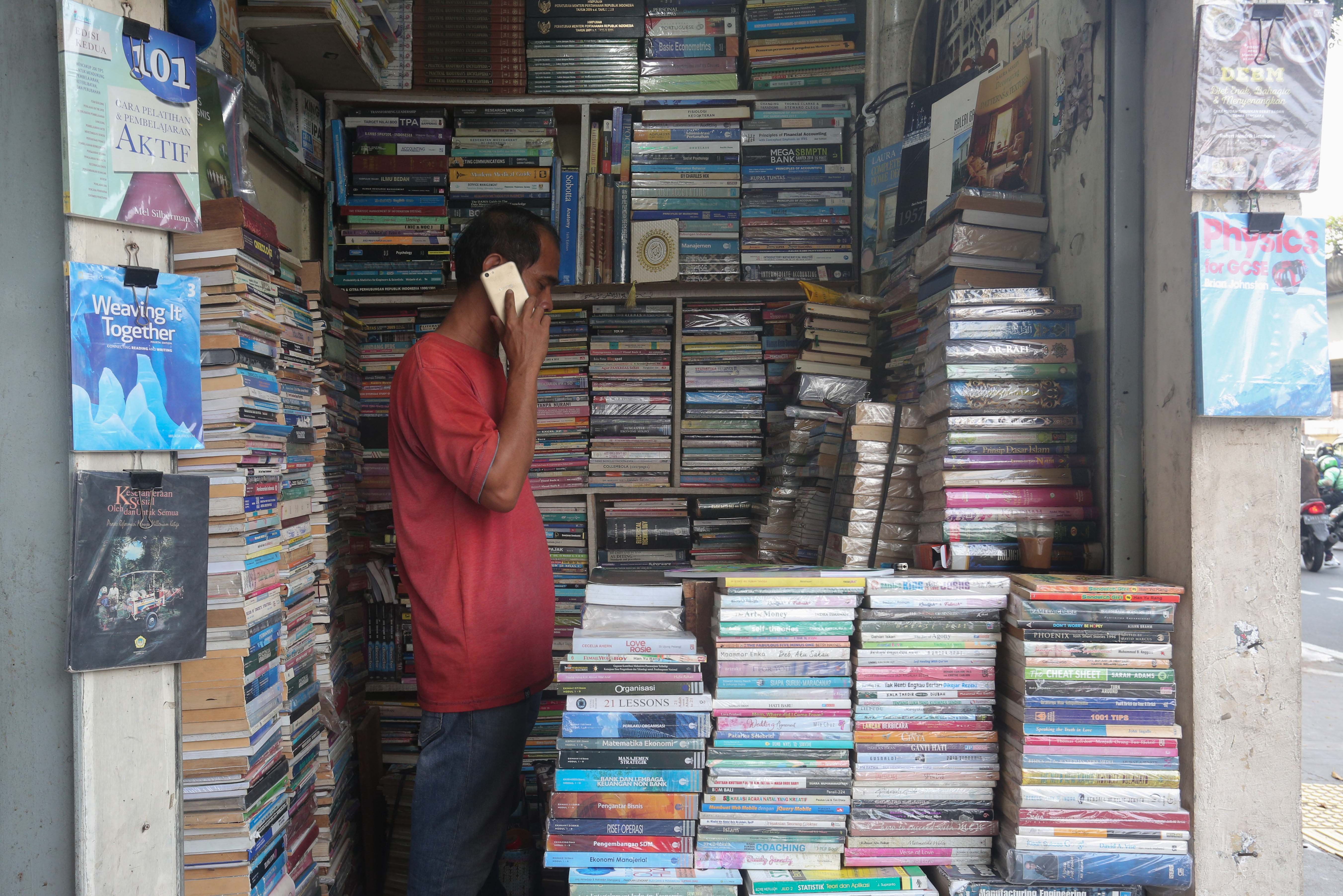 Pedagang menelpon saat menunggu pembeli di Pasar Buku Kwitang, Jakarta Pusat, Rabu (24/7/2024). Berdasarkan penuturan pedagang, berkembangnya teknologi membuat masyarakat beralih dari membaca buku fisik ke digital sehingga penjualan buku di pasar tersebut mengalami penurunan yang cukup signifikan.
