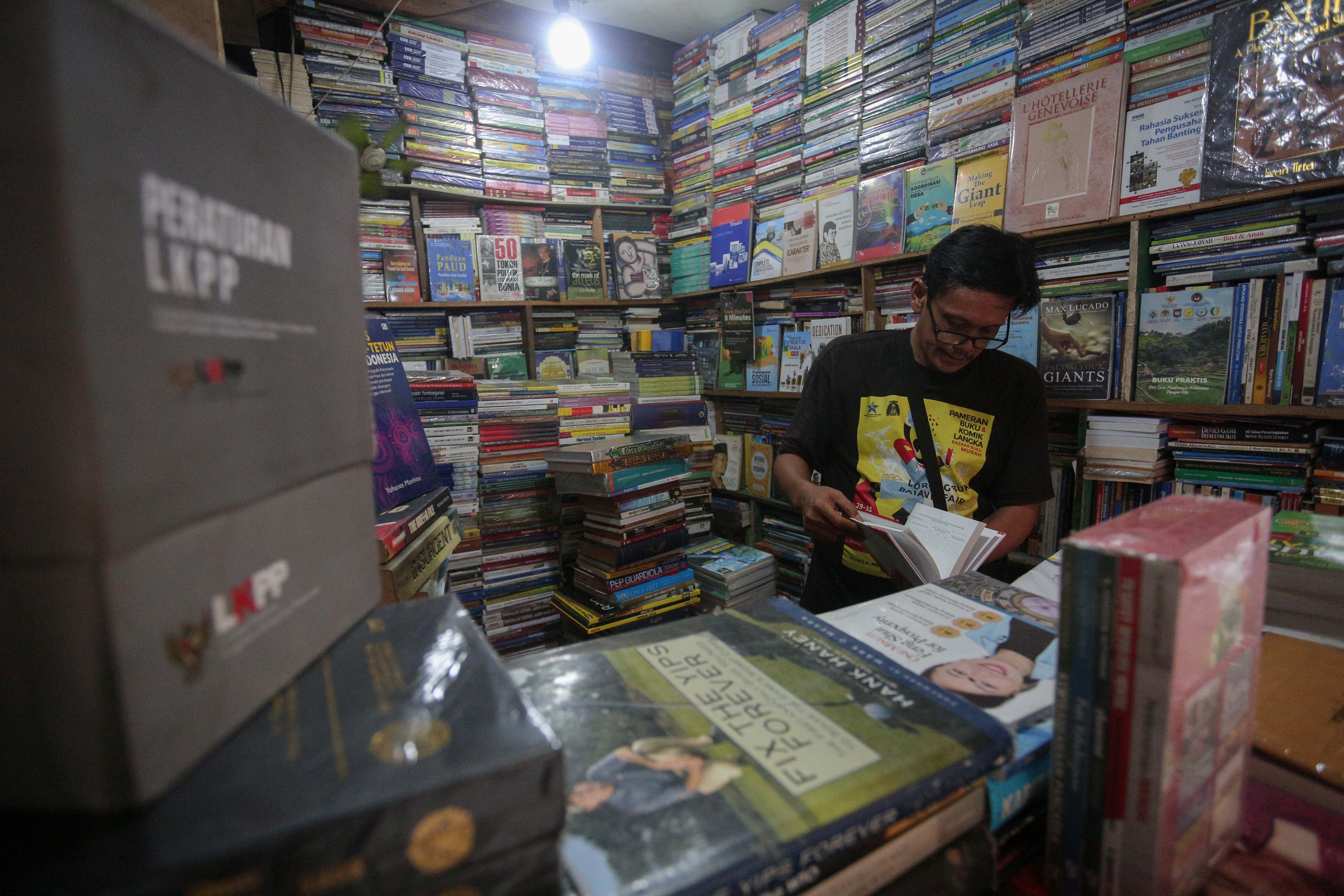 Ronald (50) melihat buku yang dijual di Pasar Buku Kwitang, Jakarta Pusat, Rabu (24/7/2024). Berdasarkan penuturan pedagang, berkembangnya teknologi membuat masyarakat beralih dari membaca buku fisik ke digital sehingga penjualan buku di pasar tersebut mengalami penurunan yang cukup signifikan.