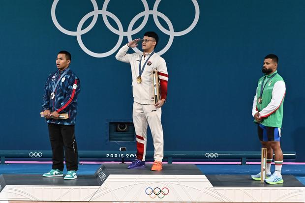 Lifter Indonesia Rizki Juniansyah (tengah) bersama lifter Thailand Wichuma Weeraphon (kiri) dan lifter Bulgaria Andreev Bozhidar Dimitrov (kanan) melakukan hormat saat upacara pengibaran bendera negara juara kelas 73 kg putra Olimpiade Paris 2024 di South Paris Arena, Paris, Prancis, Kamis (8/8/2024). Rizki meraih medali emas setelah berhasil menduduki peringkat pertama dengan total angkatan 354 kilogram, sementara Wicuma meraih medali perak dengan total angkatan 346 kilogram dan Andreev meraih merali perun