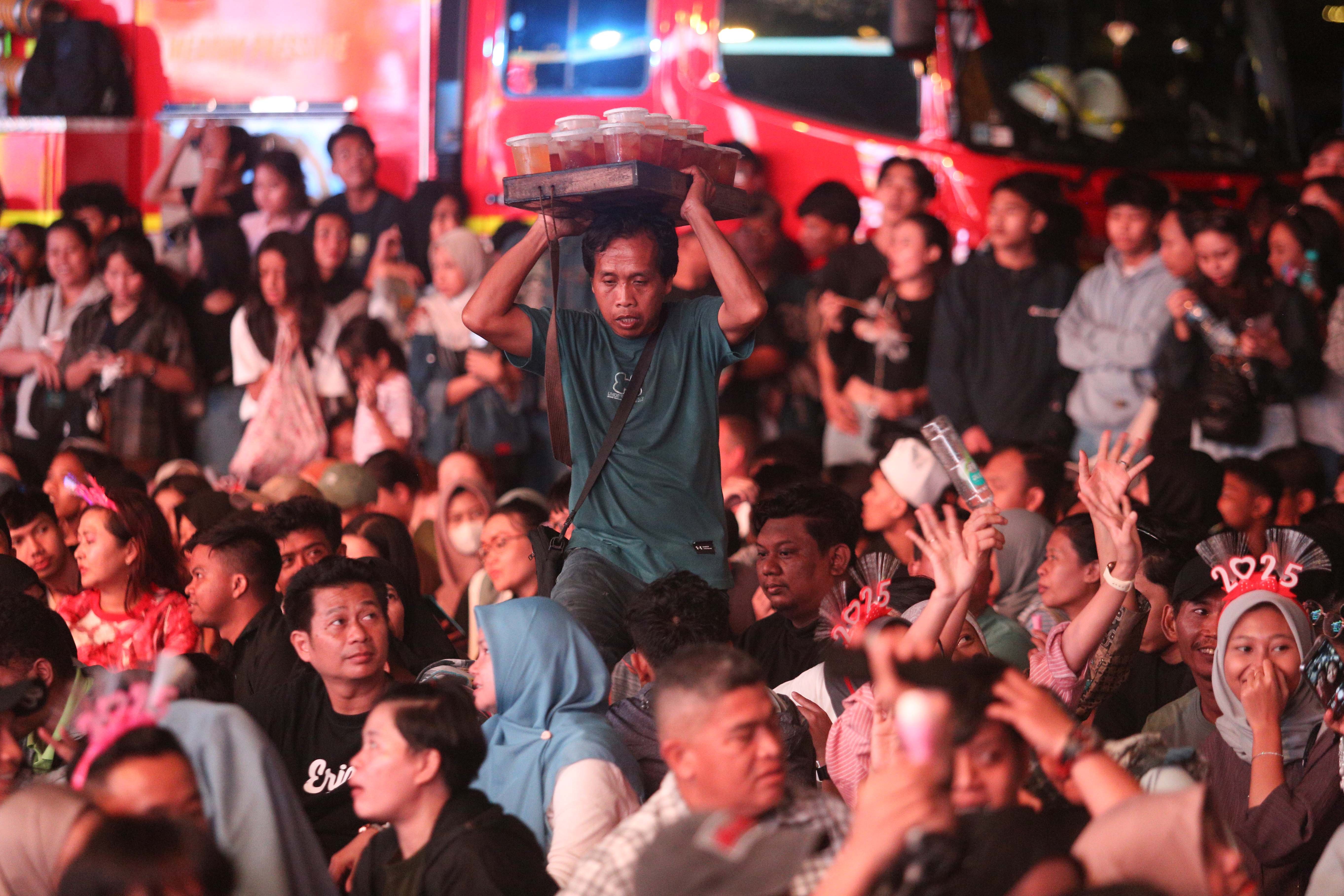 Seorang pedagang minuman menjajakan dagangannya pada acara Kirana Jakarta 2025 di Bundaran HI, Jakarta, Selasa (31/12/2024). Pemprov Jakarta menggelar perayaan malam tahun baru 2025 dengan tema Semarak Jakarta Mendunia yang diisi oleh penampilan musik dari Yura Yunita dan RAN, pertunjukkan drone hingga pesta kembang api.