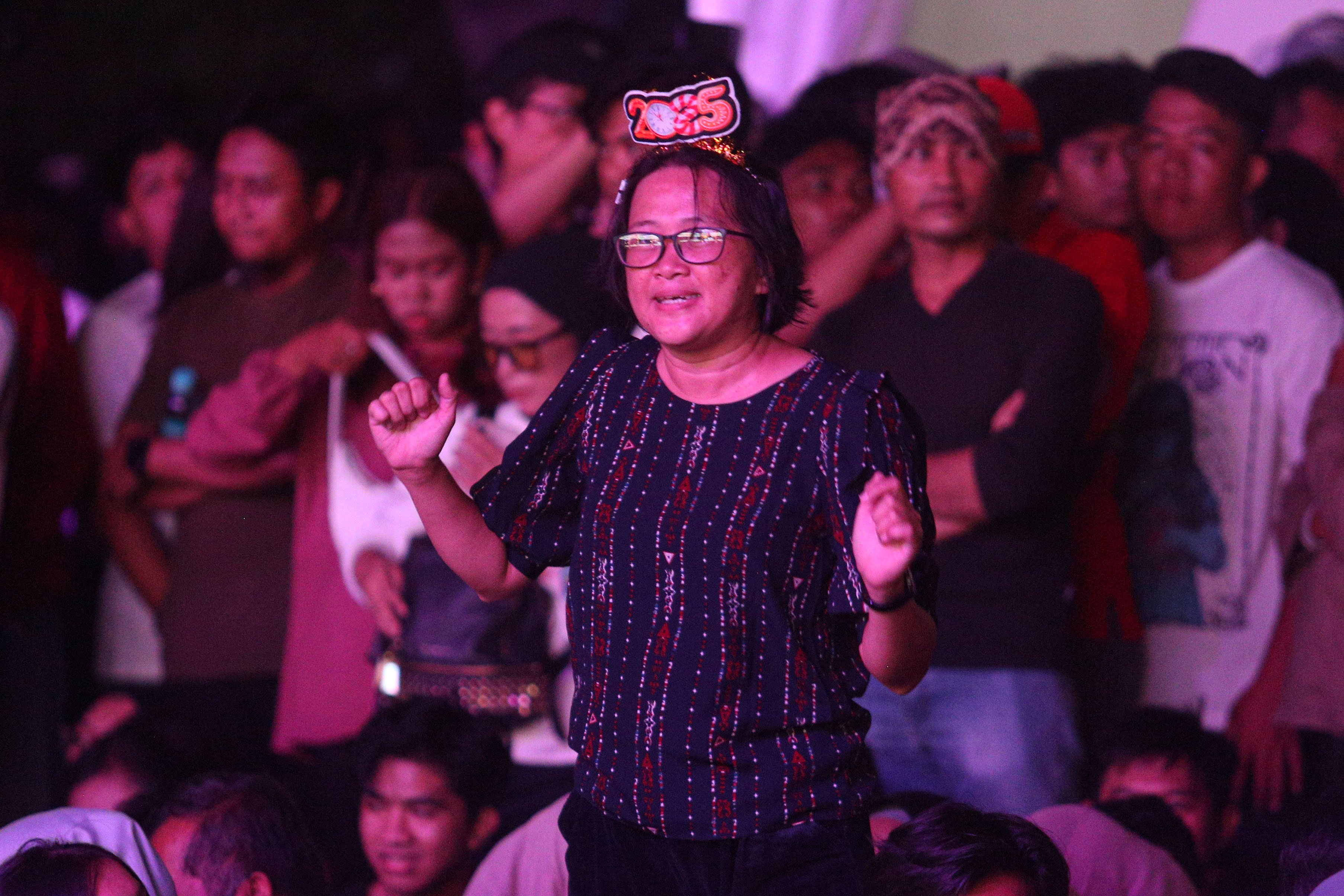 Seorang warga bernyanyi saat Yura Yunita tampil pada acara Kirana Jakarta 2025 di Bundaran HI, Jakarta, Selasa (31/12/2024). Pemprov Jakarta menggelar perayaan malam tahun baru 2025 dengan tema Semarak Jakarta Mendunia yang diisi oleh penampilan musik dari Yura Yunita dan RAN, pertunjukkan drone hingga pesta kembang api.