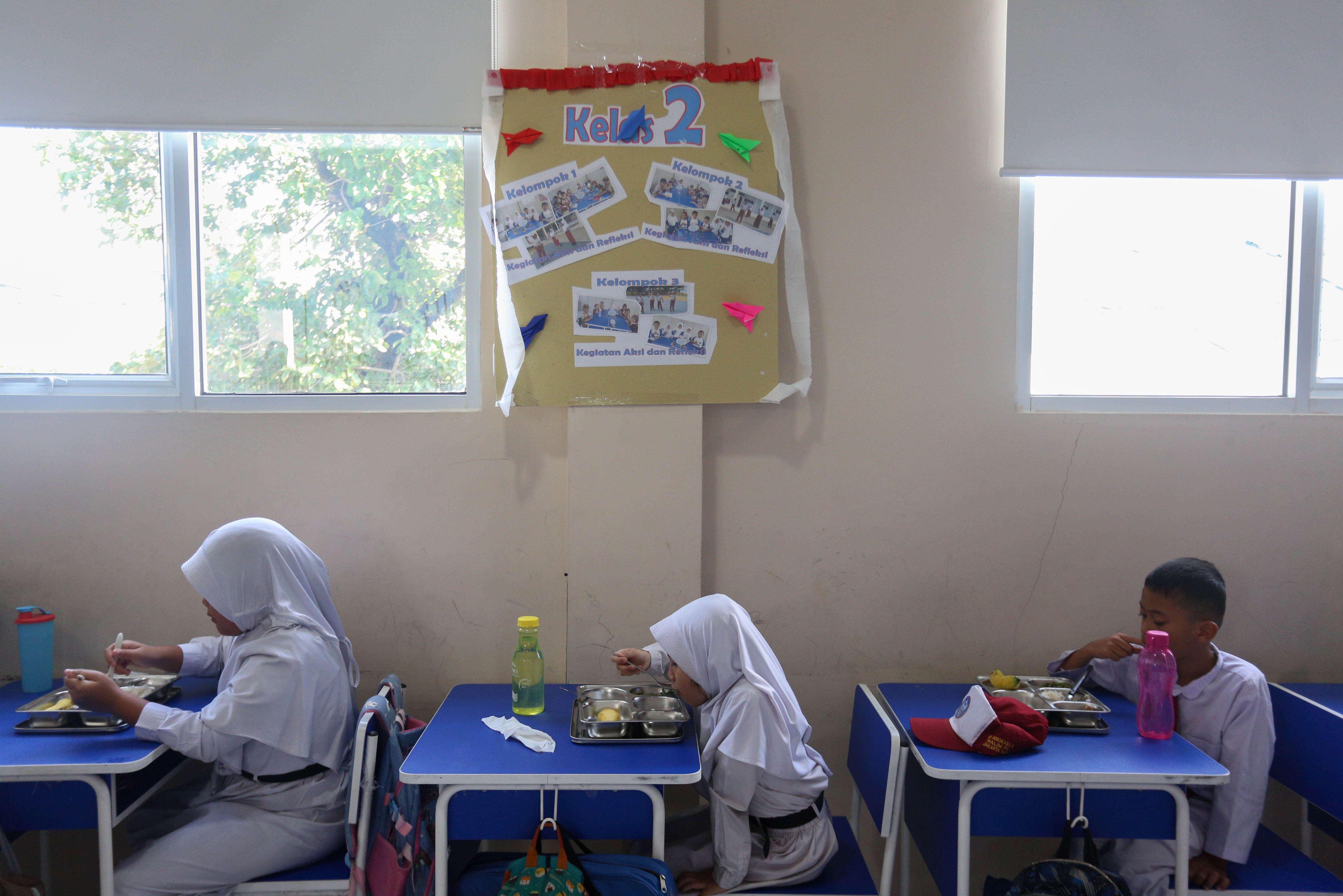 Tiga orang siswa menyantap makanan bergizi gratis di SD Angkasa 05 Halim Perdanakusuma, Jakarta Timur, Senin (6/1/2025). Pada hari pertama pelaksanaan Program Makan Bergizi Gratis di sekolah tersebut diikuti oleh 128 siswa dengan menu makanan yang dihidangkan yaitu nasi, tumis buncis, ayam saus teriyaki dan buah pisang.