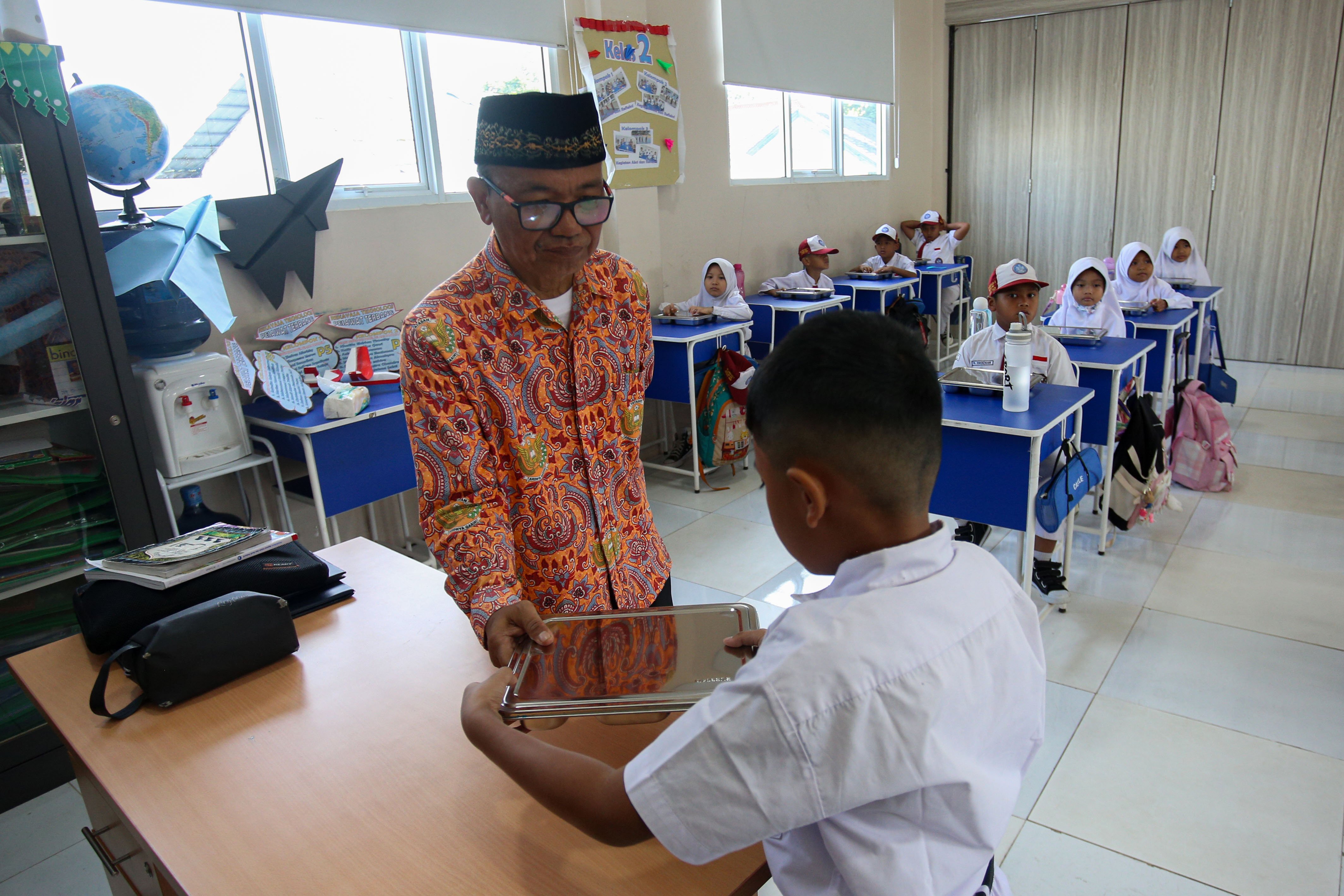 Seorang guru memberikan makanan bergizi gratis di SD Angkasa 05 Halim Perdanakusuma, Jakarta Timur, Senin (6/1/2025). Pada hari pertama pelaksanaan Program Makan Bergizi Gratis di sekolah tersebut diikuti oleh 128 siswa dengan menu makanan yang dihidangkan yaitu nasi, tumis buncis, ayam saus teriyaki dan buah pisang.